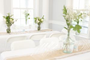 Elegant table setting with glass vases holding fresh greenery and flowers in a bright sunlit room.