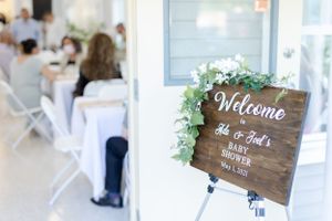 Rustic wooden welcome sign decorated with greenery at an event entrance.