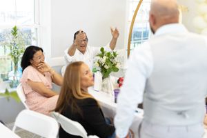 Party guests engage in animated conversation and laughter at a bright indoor event.