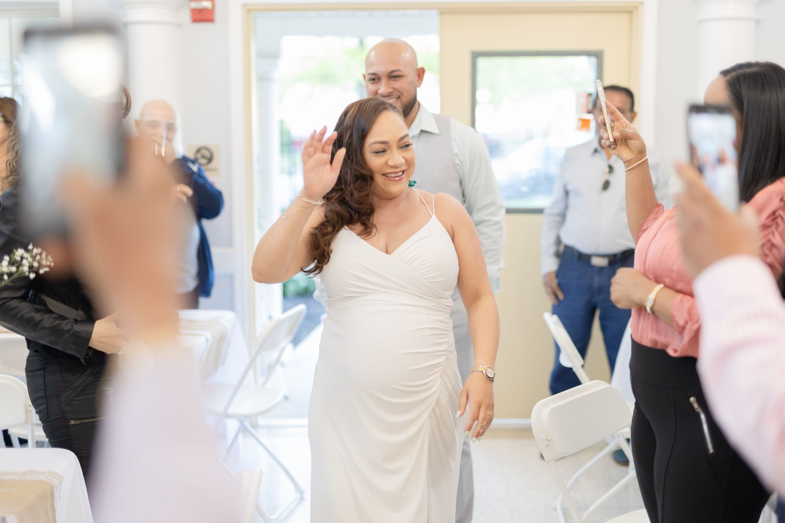 A person in an elegant white gown waves to guests during a celebratory event.