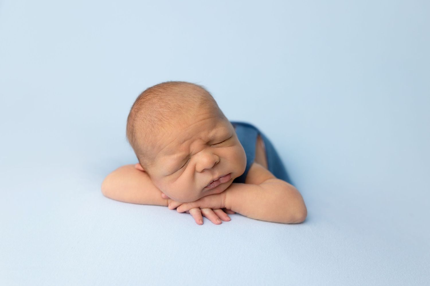 Sleeping newborn in blue wrap laying on light backdrop during studio photography session.