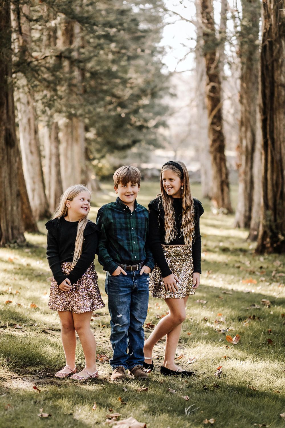 Three children pose together on a wooded path during golden hour.