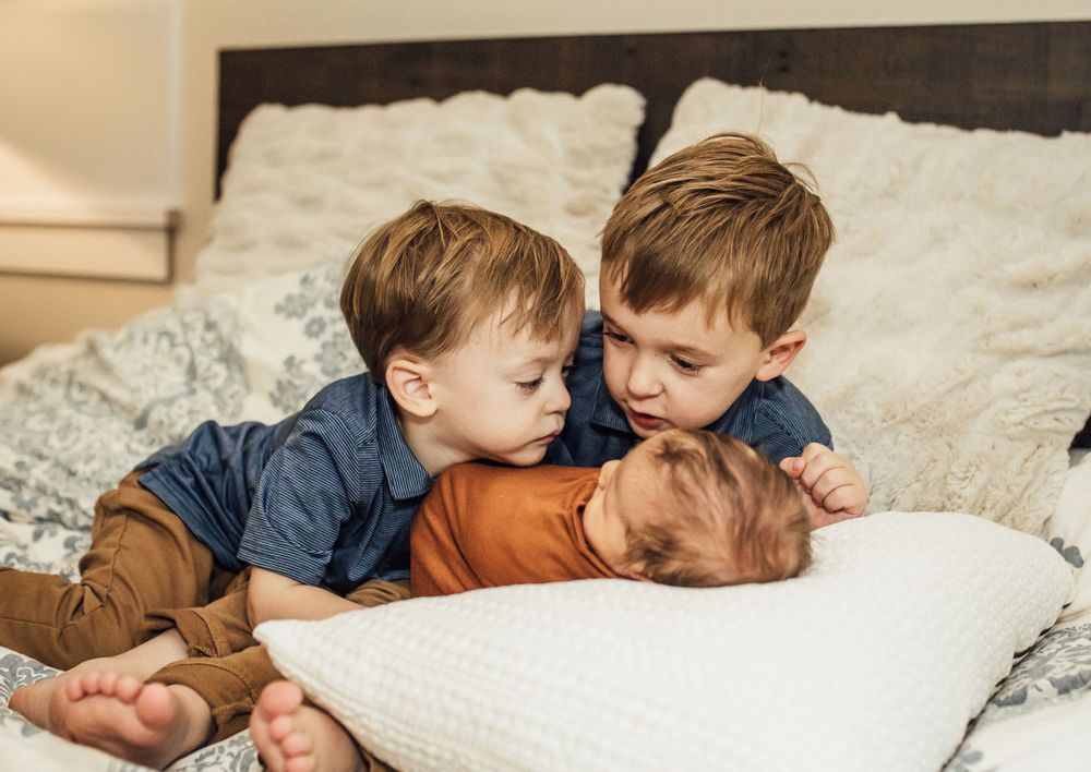 Three young children cuddling and playing together on a white cushioned couch.