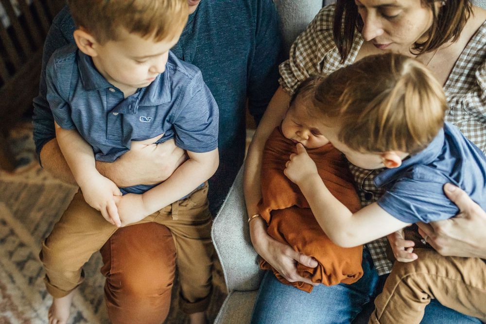 Two children in denim shirts reading books together with someone on a comfortable couch at home.
