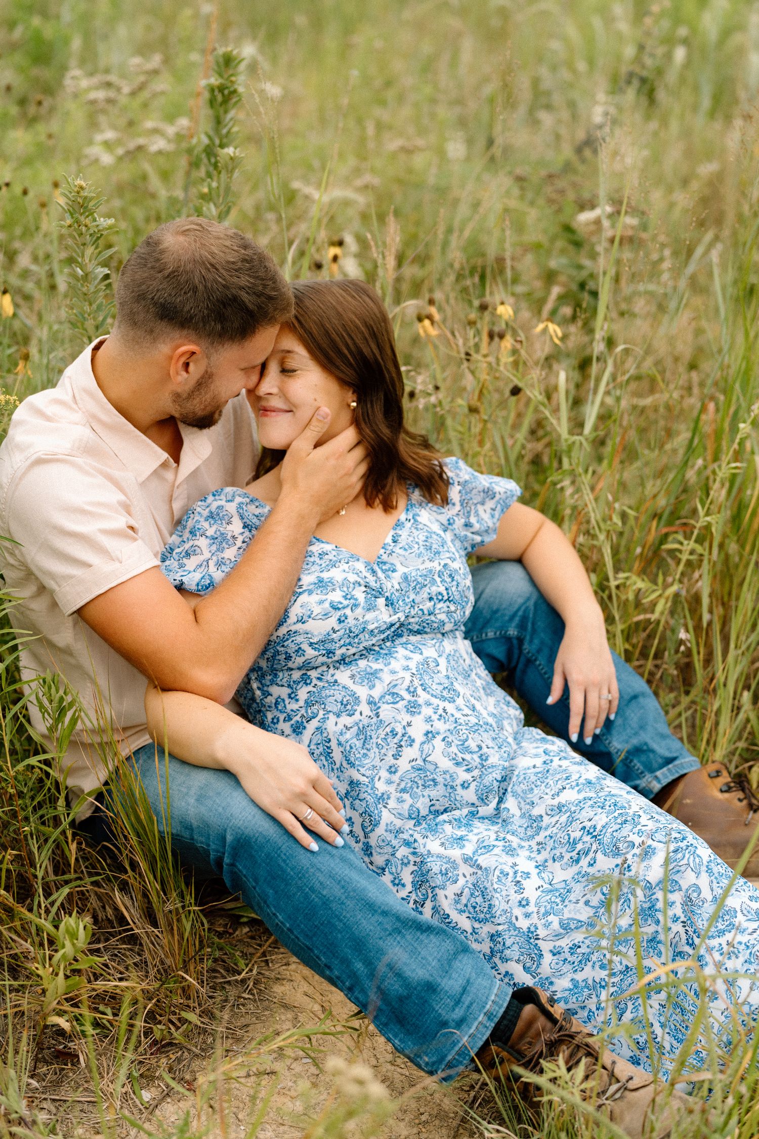 A couple embraces lovingly in a wildflower meadow while wearing coordinating summer outfits.