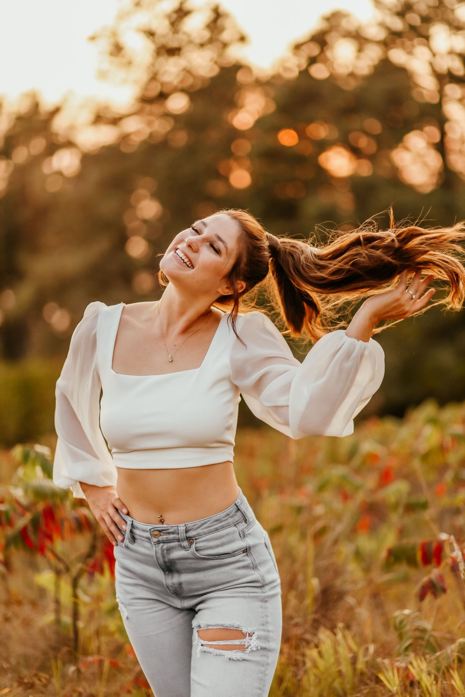 Woman in white crop top dancing joyfully at sunset with hair flowing in the wind.