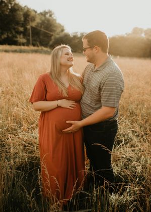 Couple gazing at each other lovingly in a golden wheat field during a warm sunset maternity session.