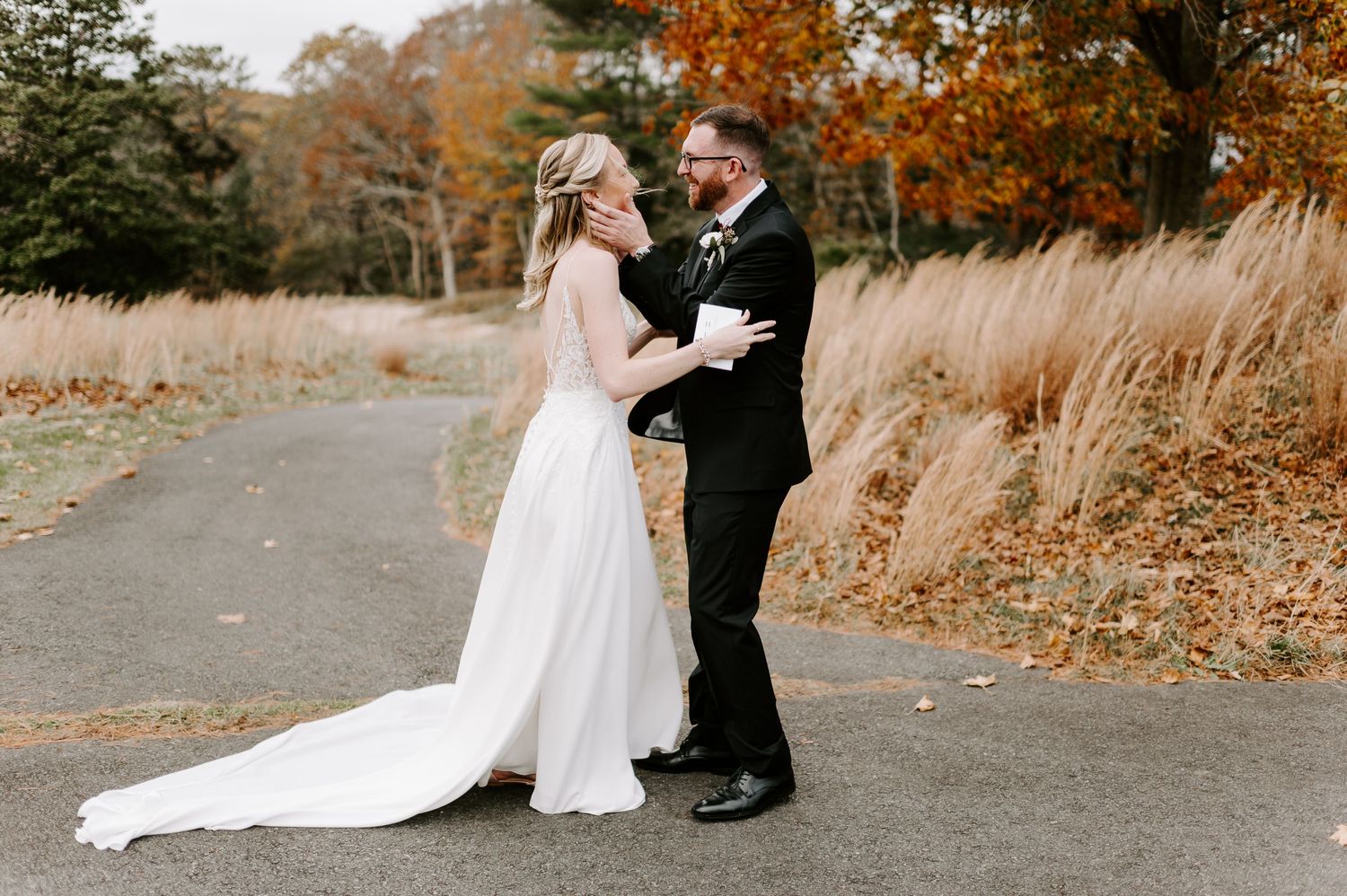 Romantic wedding couple poses on path surrounded by autumn foliage and golden light.
