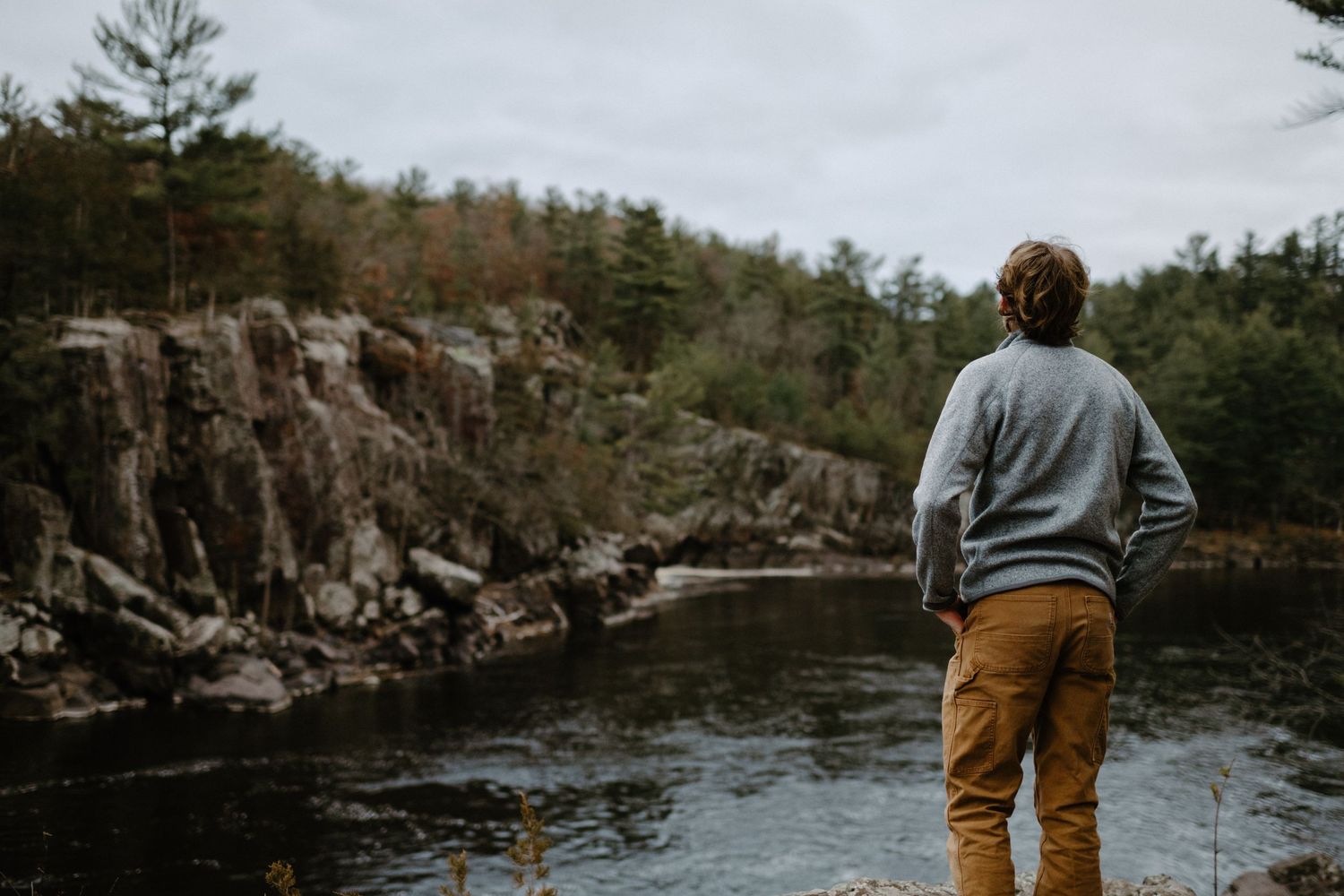 Moody landscape shot of someone overlooking a rocky river gorge surrounded by pine trees.