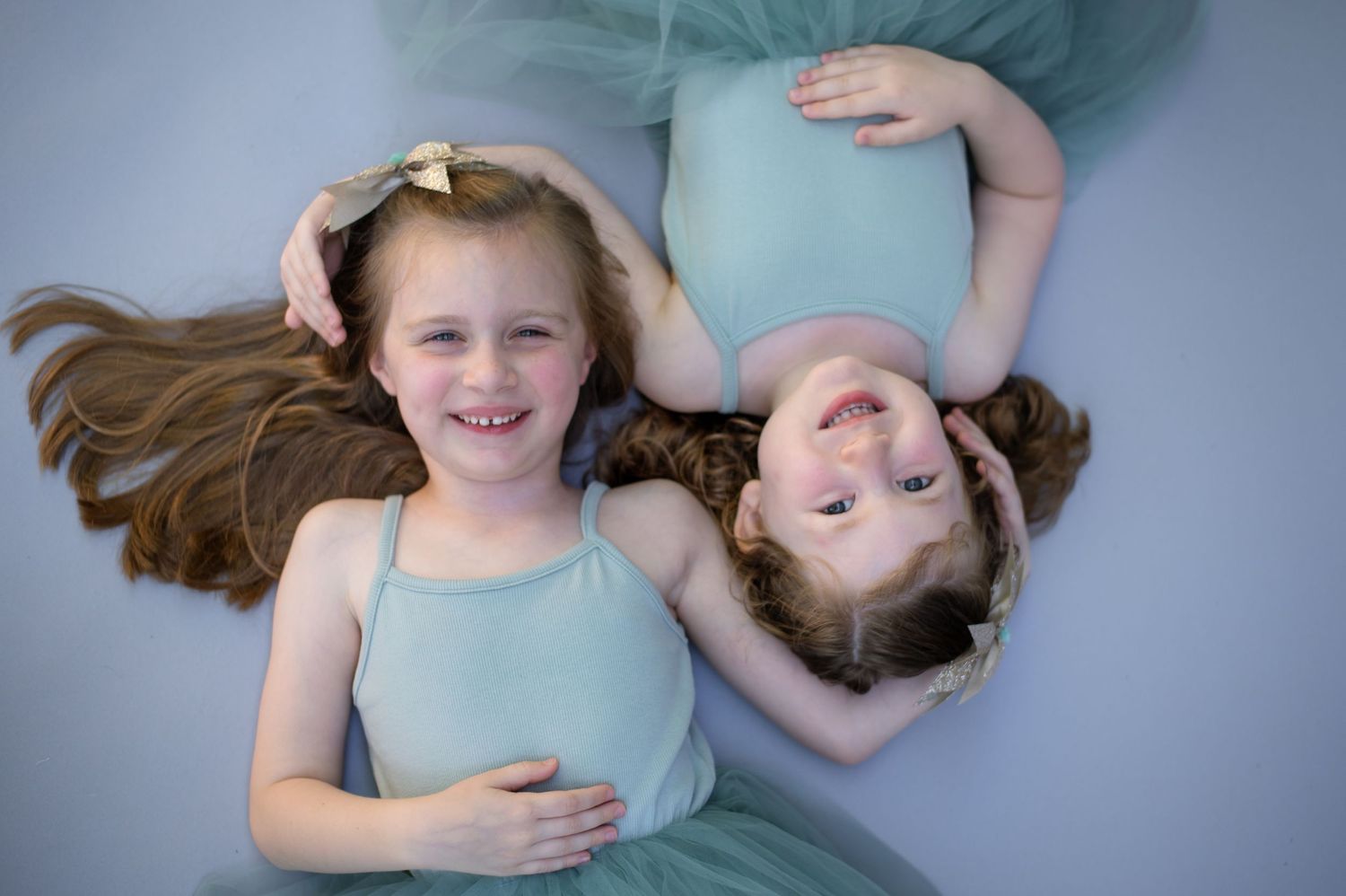 Two dancers in matching mint colored dresses lying on a gray floor with long hair spread out.