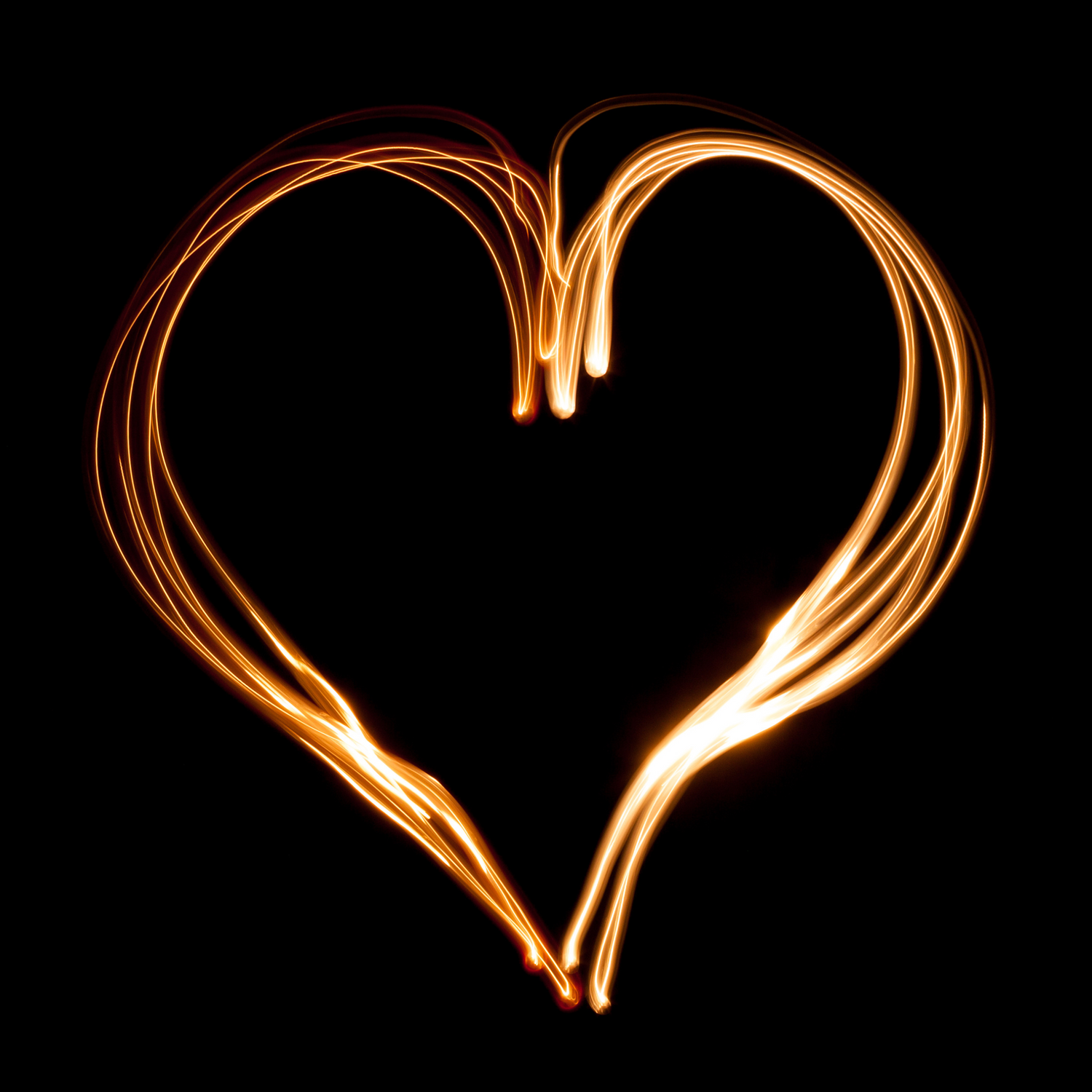 Long exposure light painting creating heart shapes in golden light against dark background.