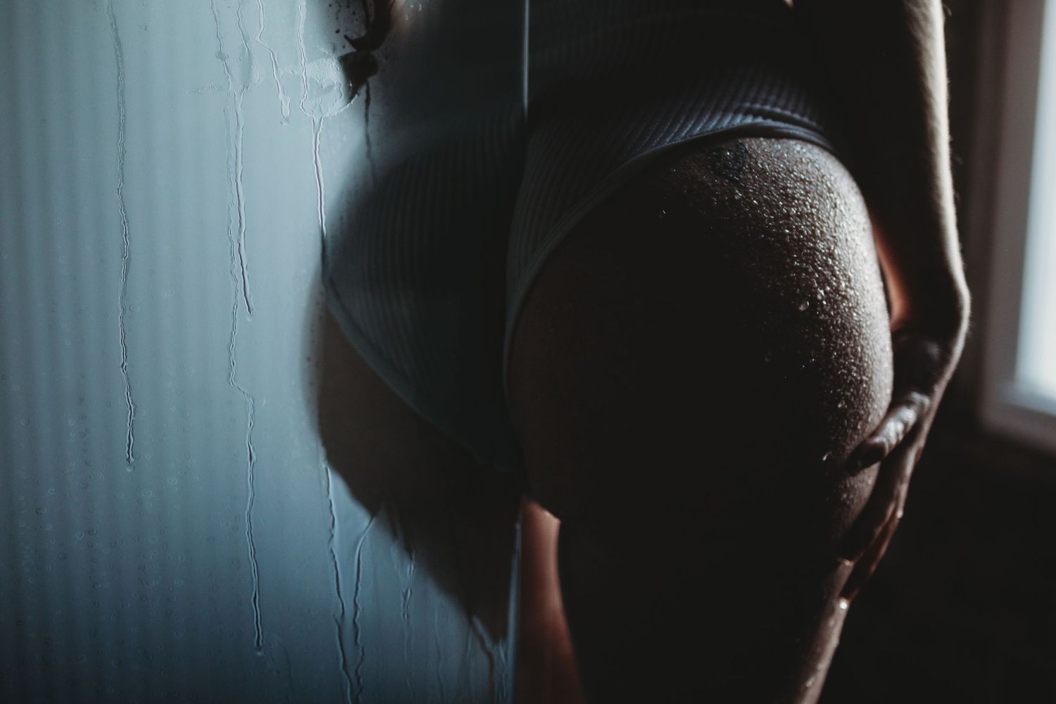 Artistic silhouette portrait of a pregnant woman's belly in moody lighting near a window.