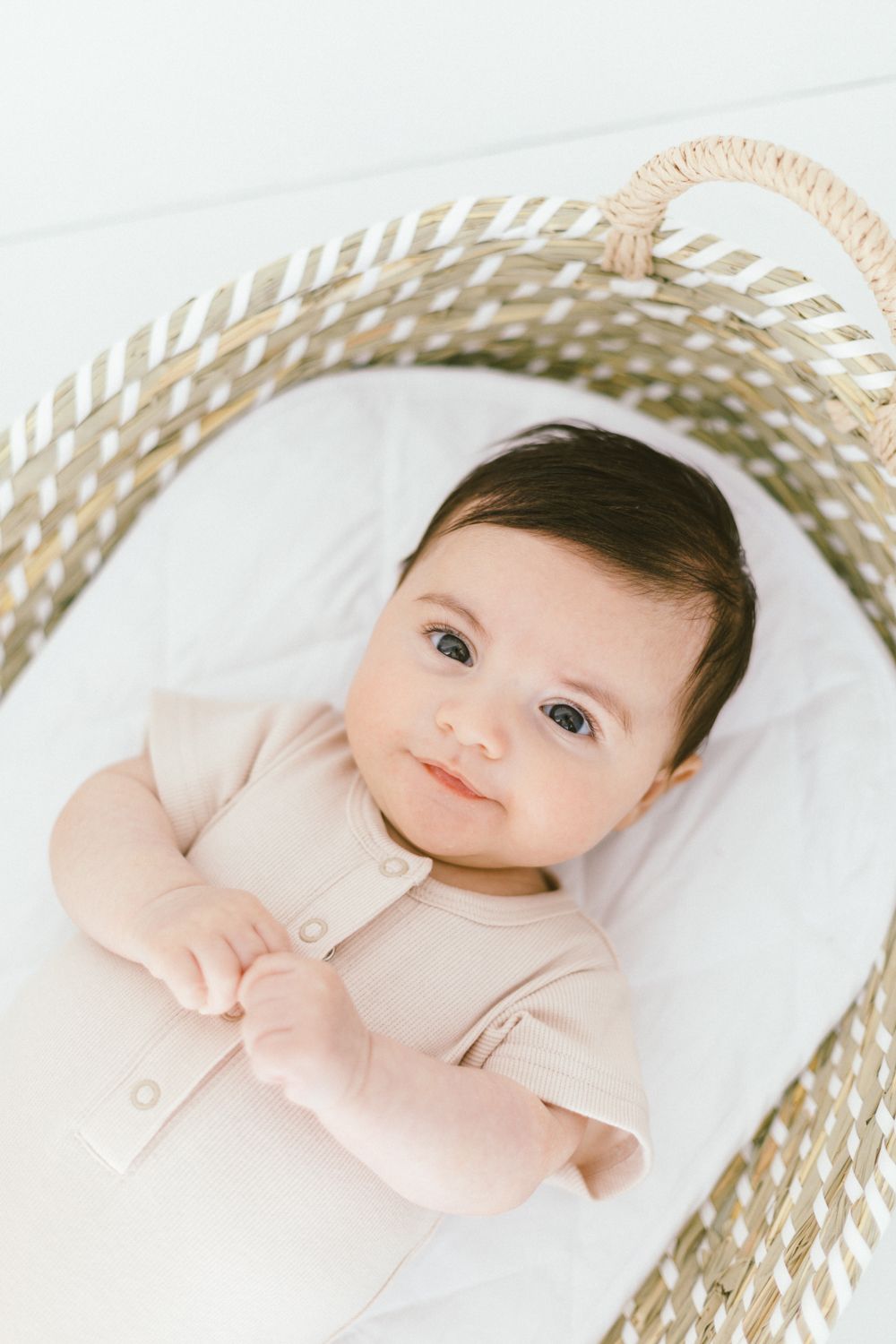 Baby in beige onesie lying in woven basket with white lining.
