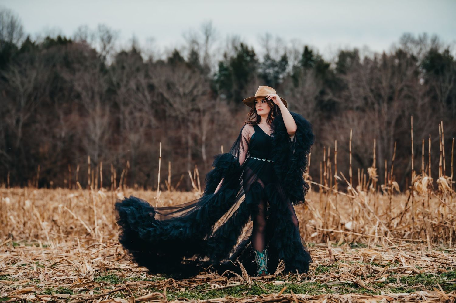 Dramatic outdoor portrait in flowing black dress against autumn field backdrop.