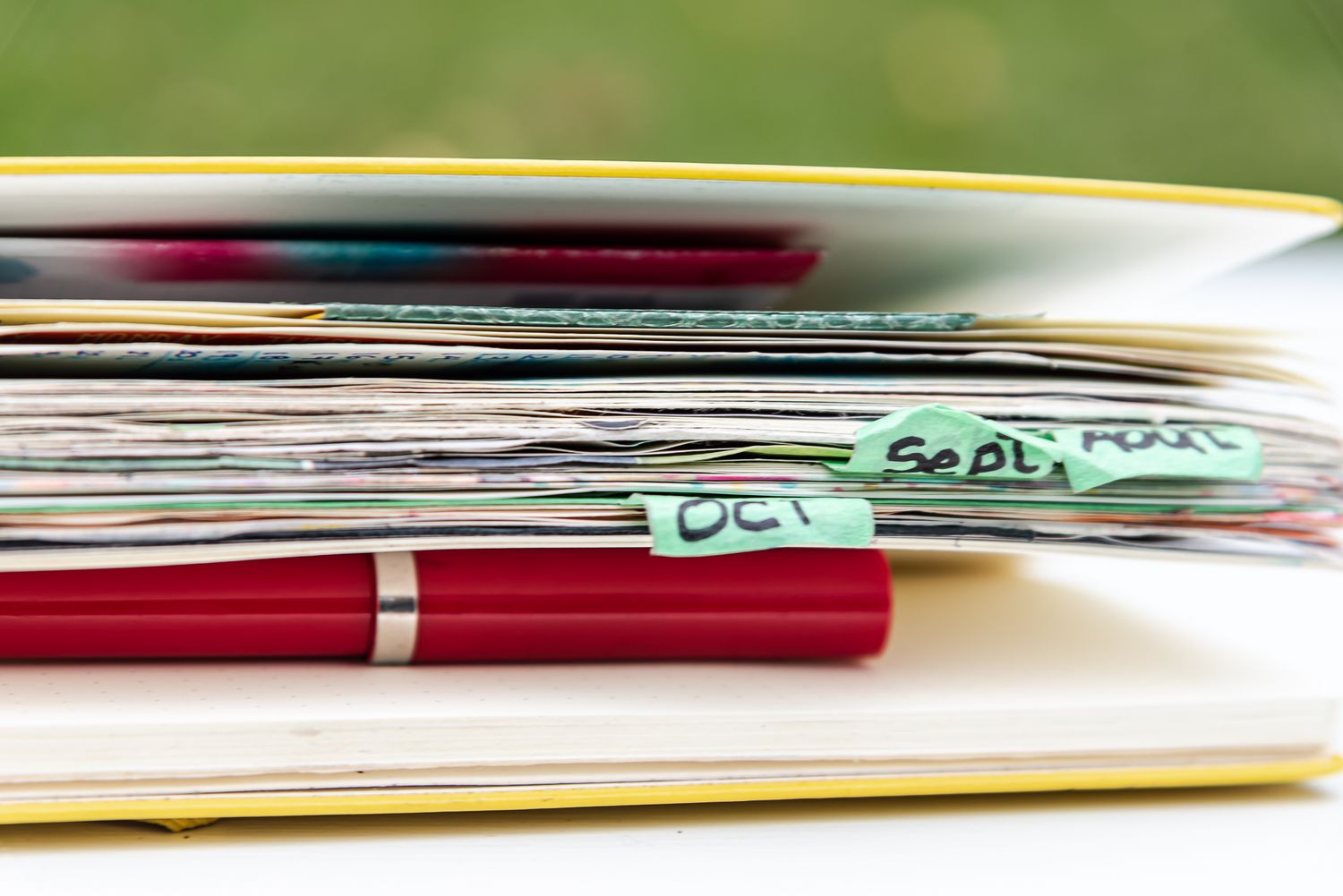 Closeup of a red pen next to a stack of papers with colorful sticky note tabs sticking out.