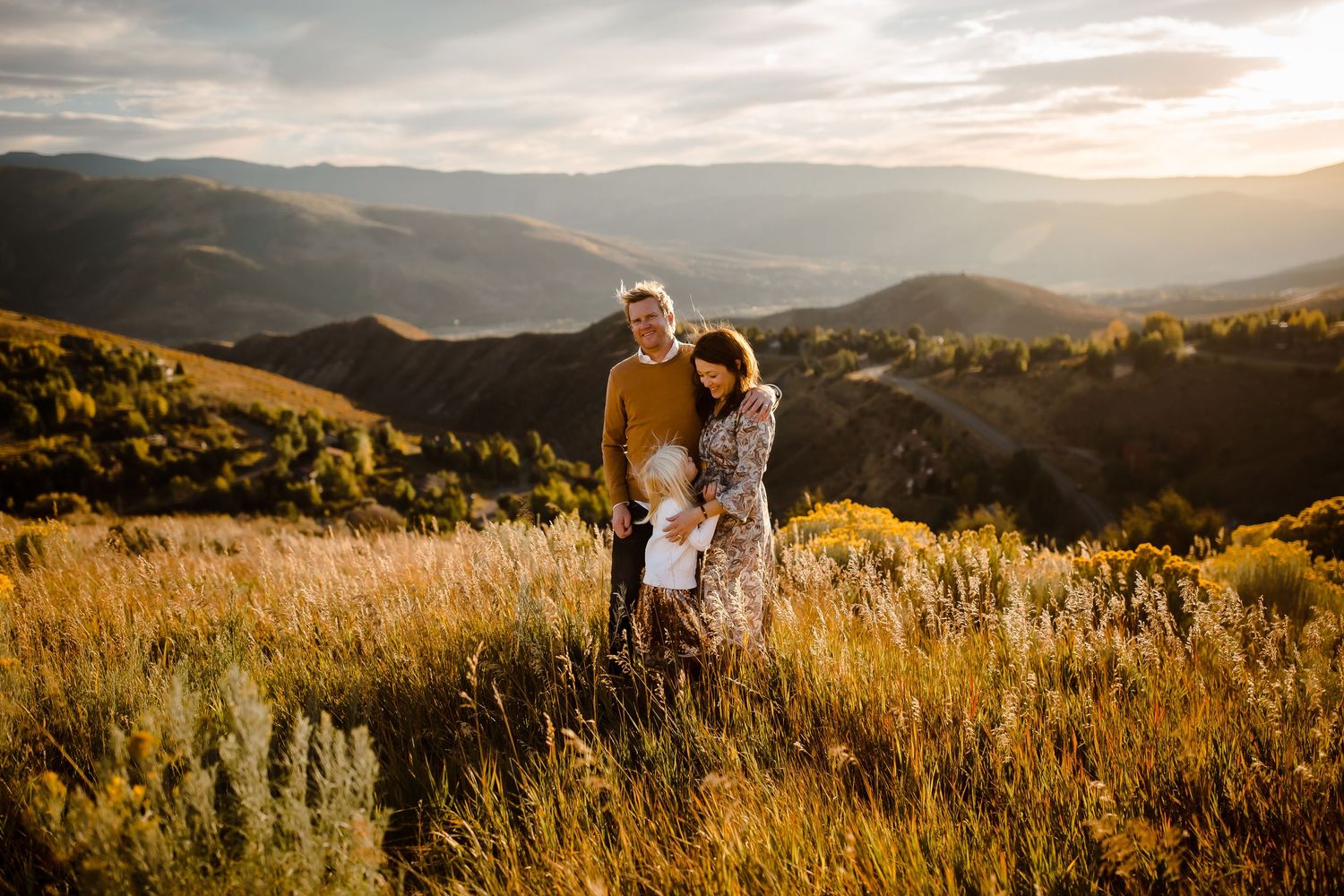 Candid family of three smiling together at sunset in open Vail Valley field