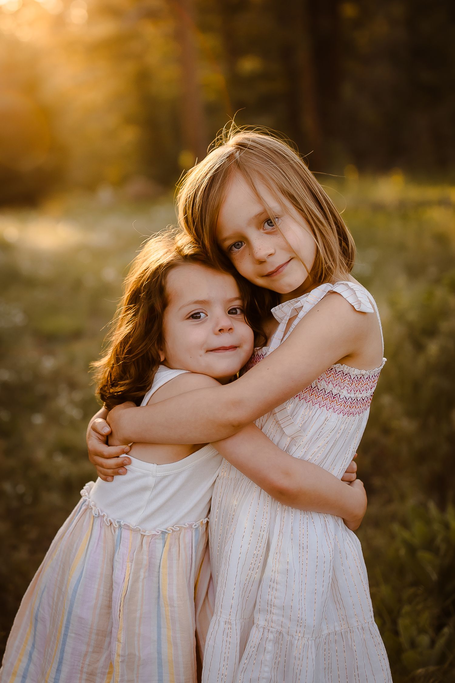 Two children embrace and smile naturally in Denver field with golden light behind them