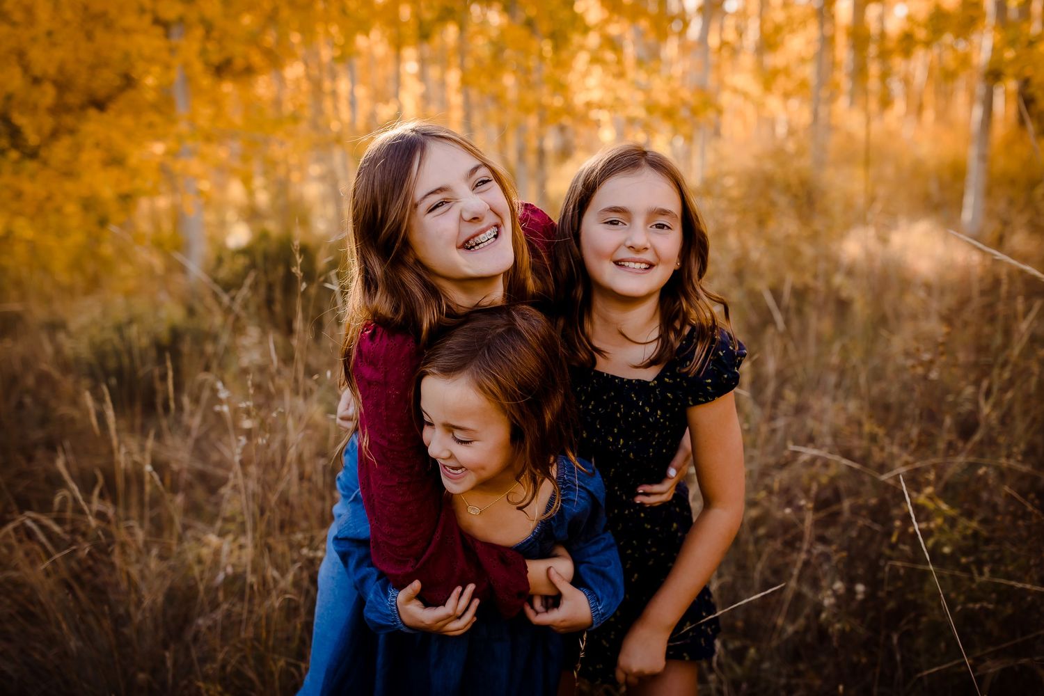 Three children laugh candidly in front of golden aspen trees