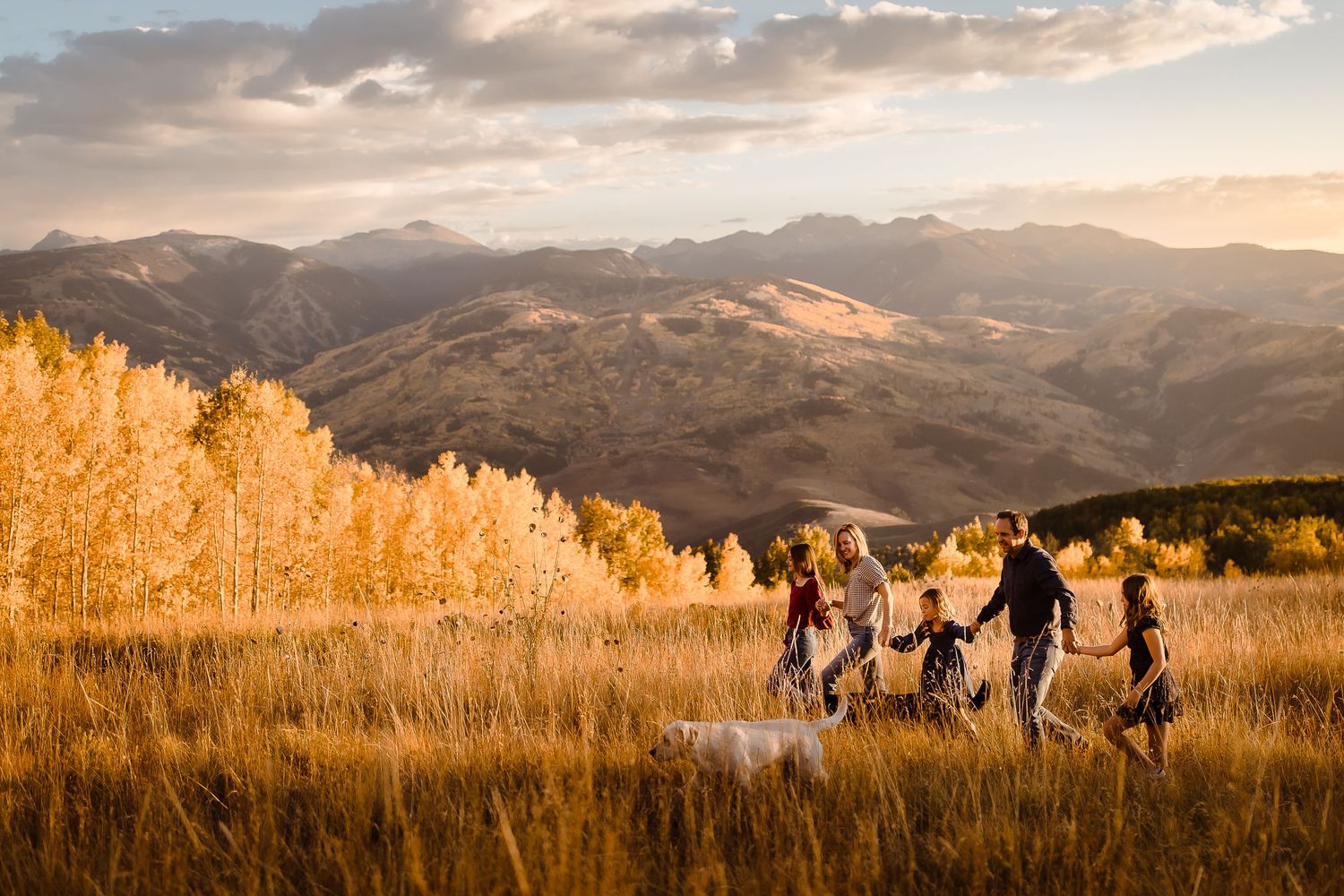 A family of five walks through a golden field in Vail Colorado with sweeping mountain views behind them