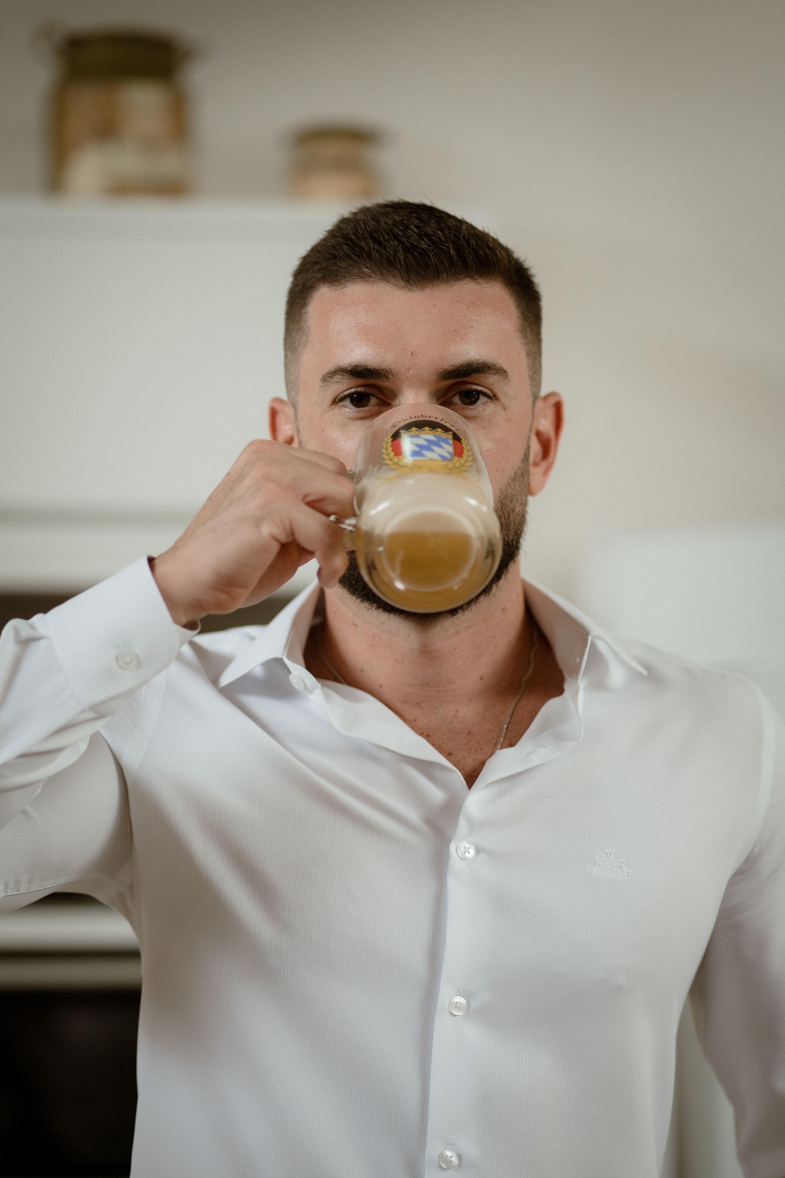 Person in white shirt drinking from a glass mug in a kitchen setting.