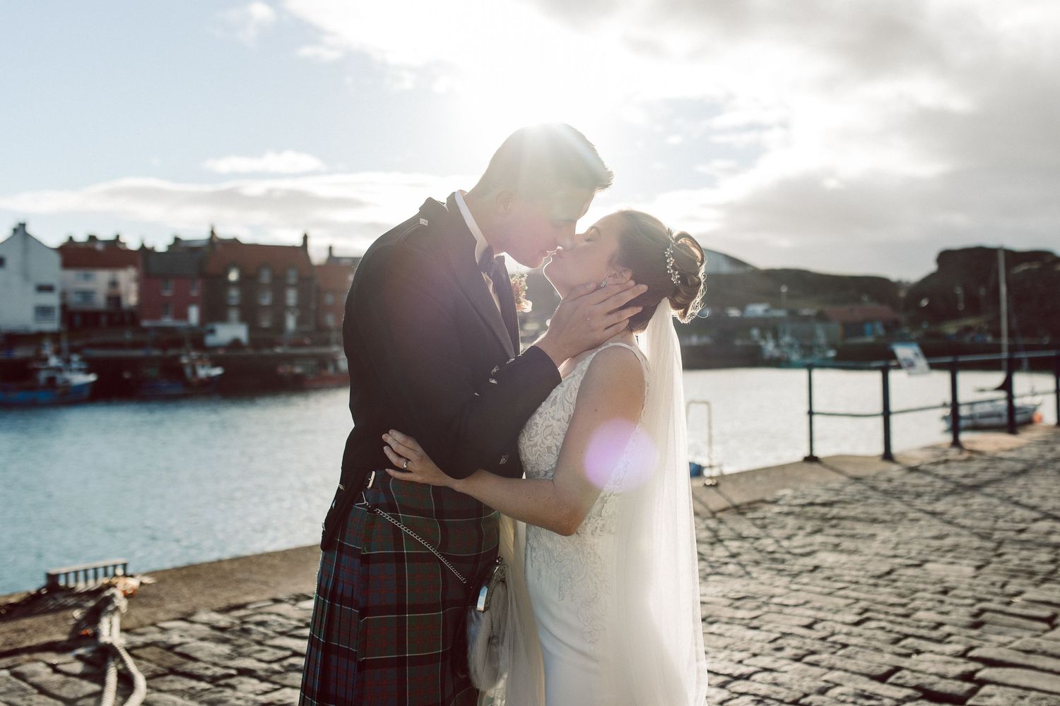 A couple stands on cobblestone streets by the waterfront during a sunset photo session.
