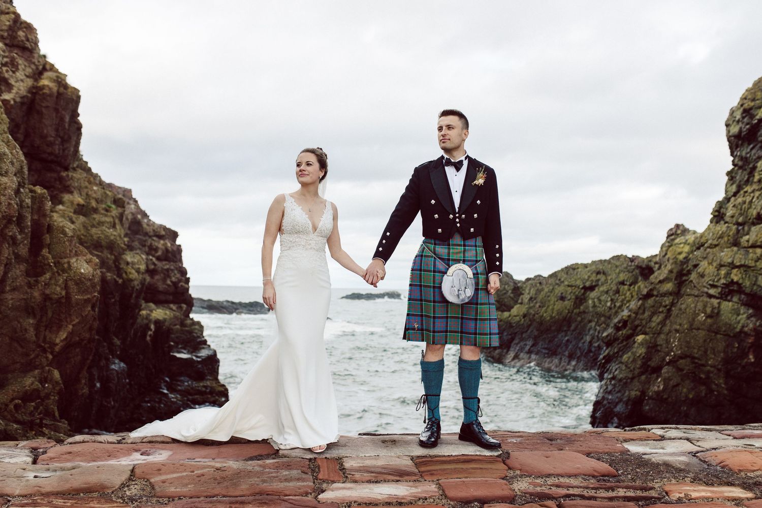 Dramatic coastal wedding photos with rocky cliffs and ocean waves in the background.