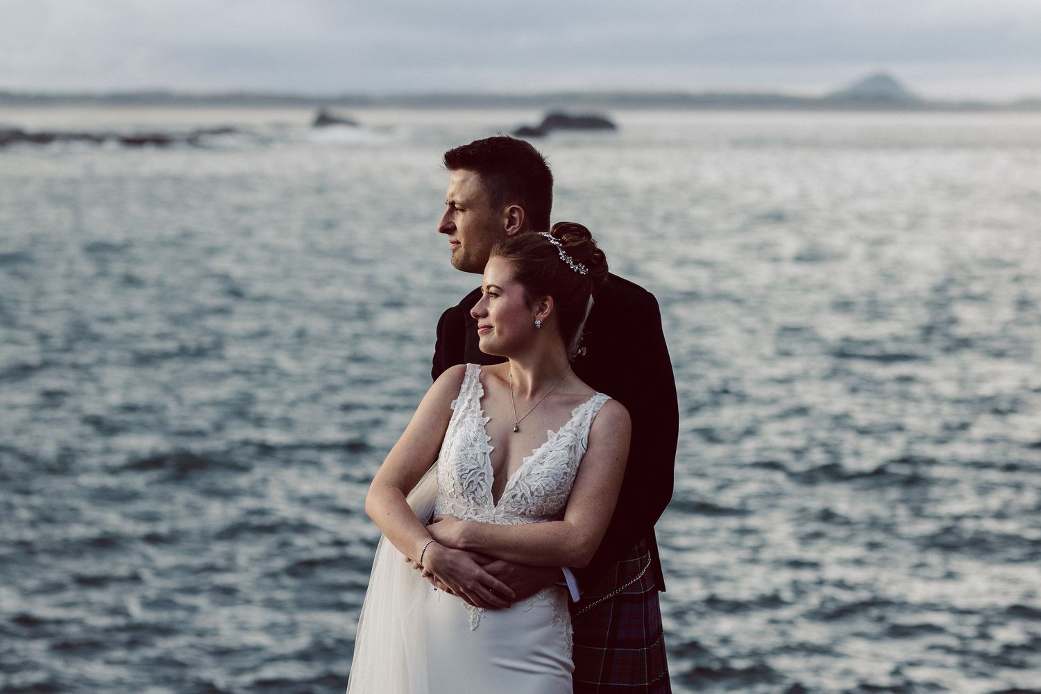 Wedding couple poses along dramatic seaside cliffs with waves crashing below.