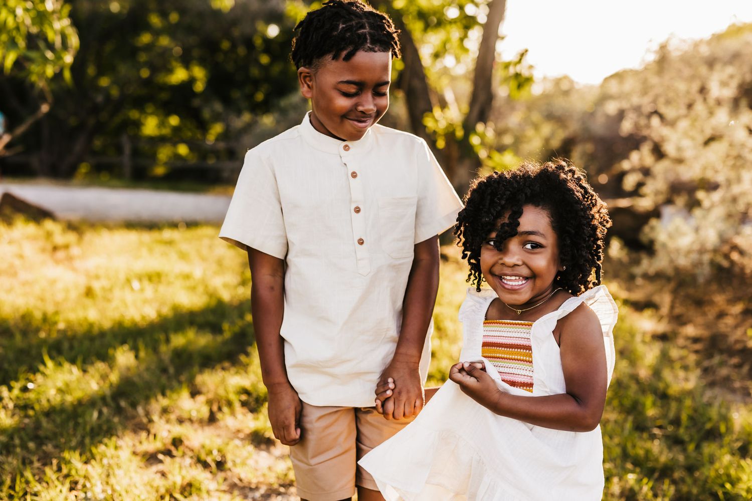 Two children in white outfits sharing a joyful moment outdoors in golden sunlight.