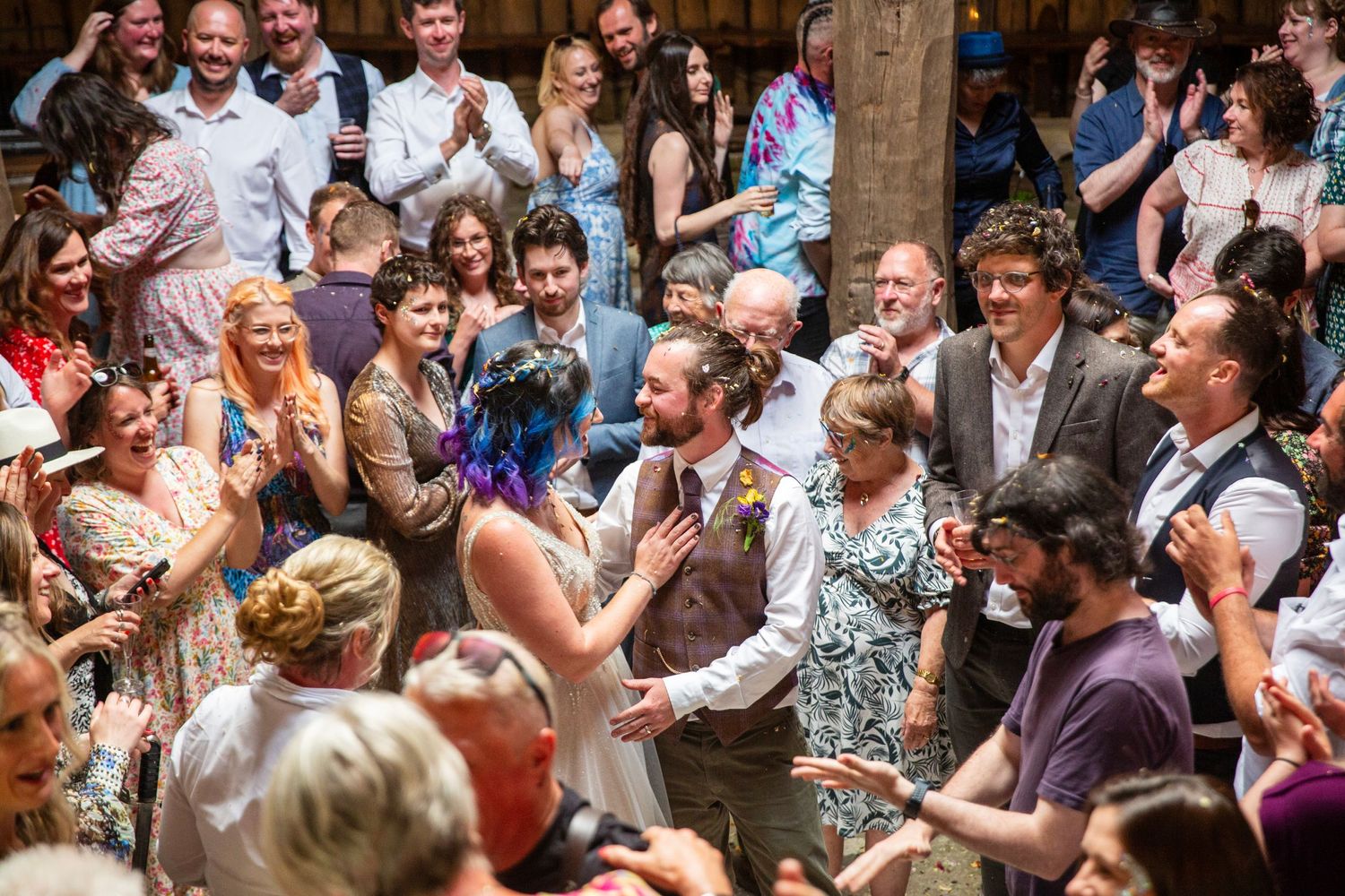 Energetic wedding reception with guests dancing and celebrating in a rustic indoor space.