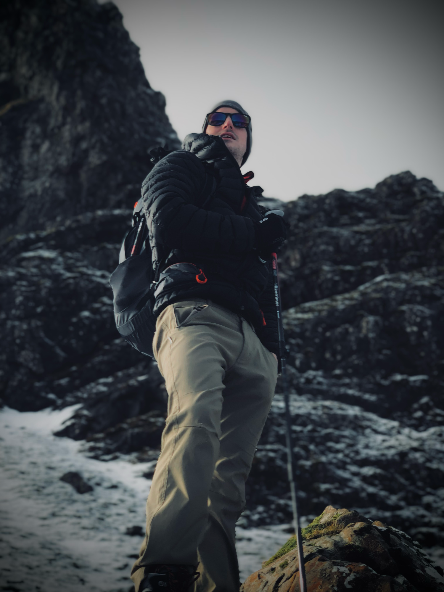 Hiker in winter gear standing on snowy rocks against dramatic mountain backdrop.