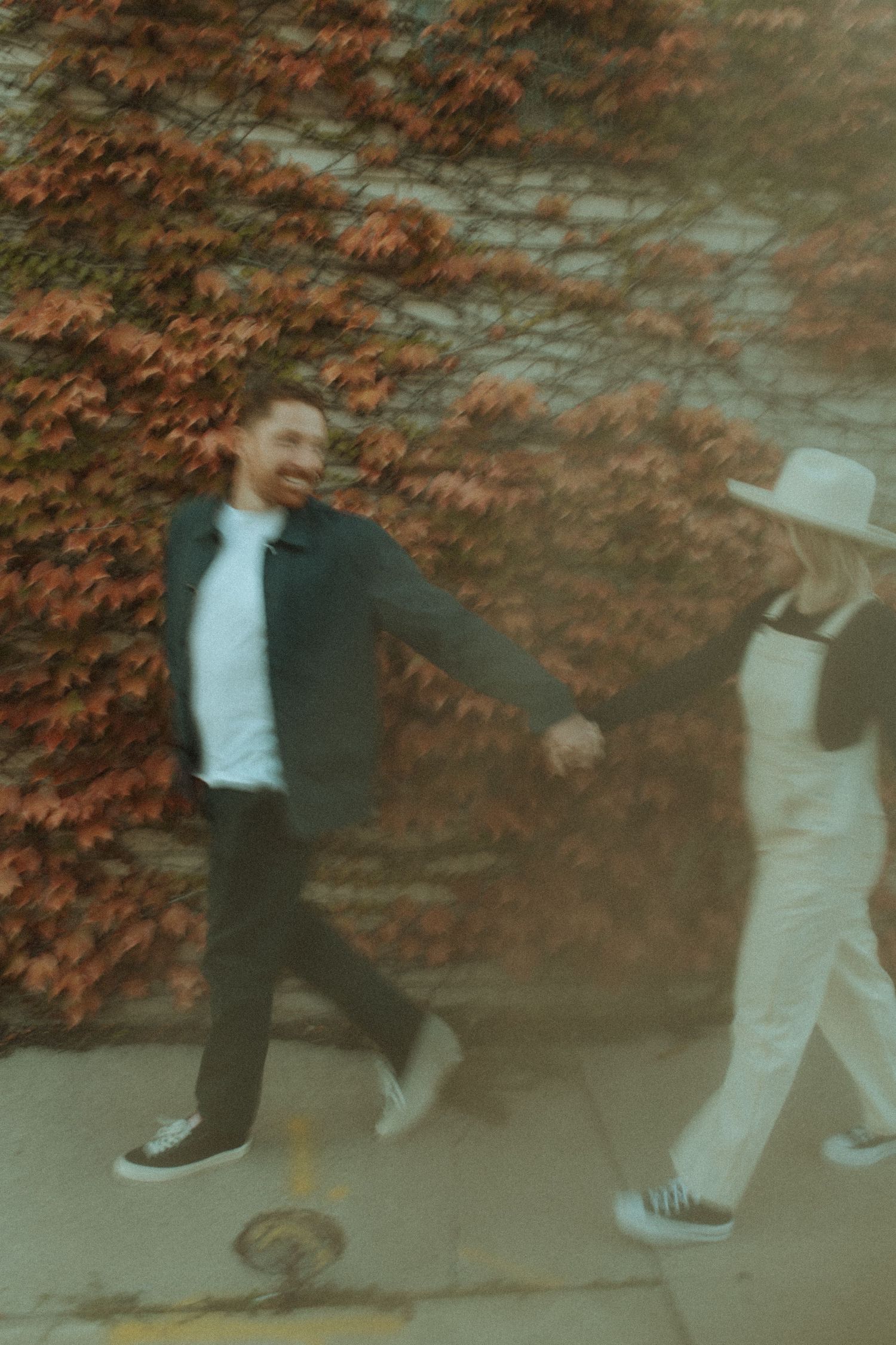Playful moment captured between two people walking by autumn ivy wall.