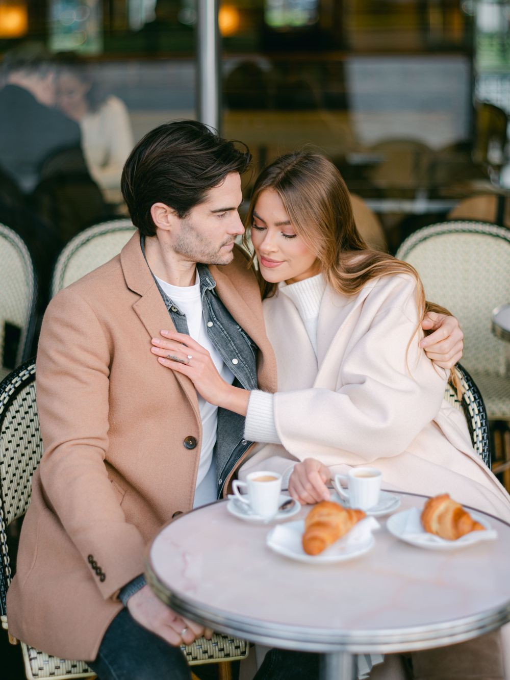 Un couple partageant un moment intime dans un café parisien, avec des croissants et du café.