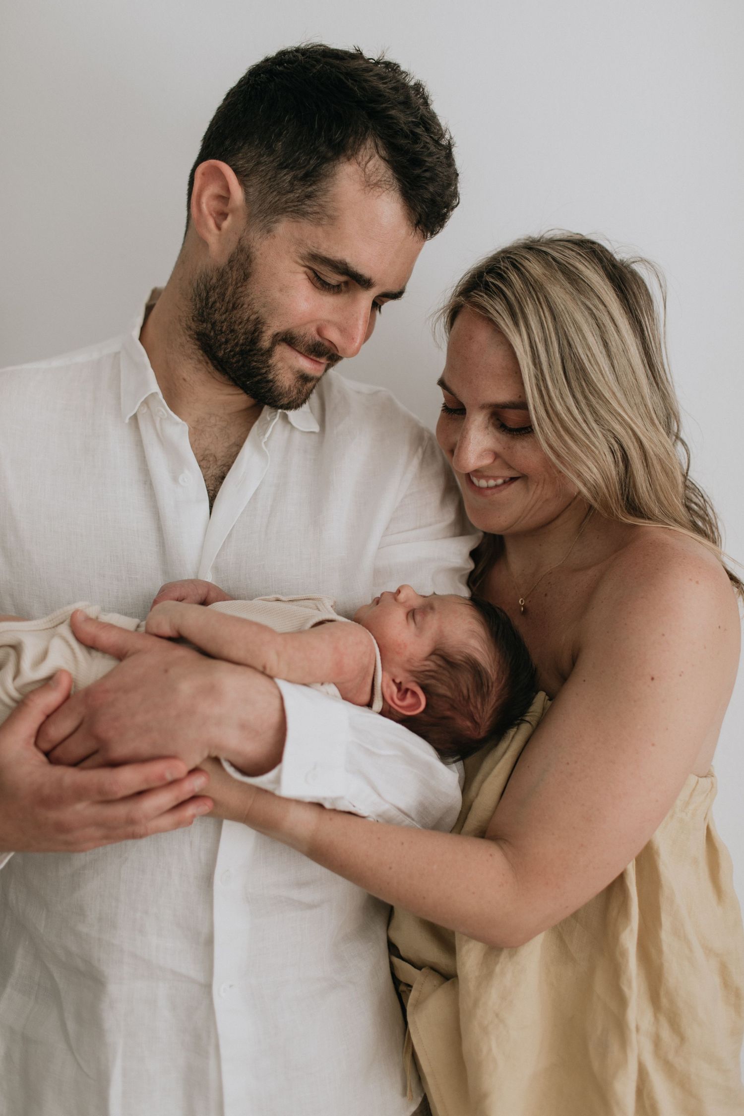 Couple in neutral tones tenderly holding sleeping newborn baby.