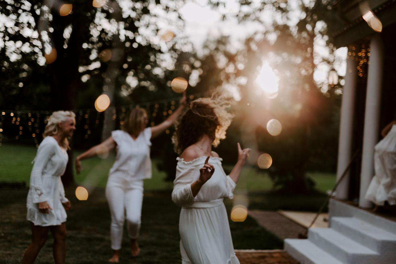 Wedding guests dancing and celebrating outdoors at sunset with bokeh lights.