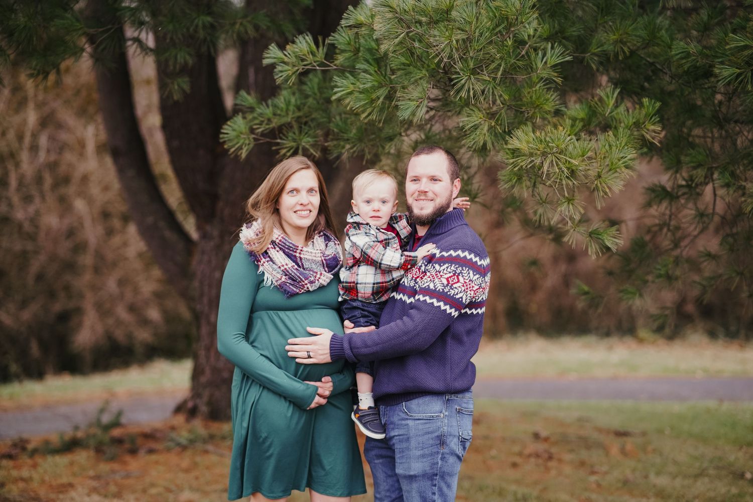 Winter family portrait with evergreen trees and coordinating sweaters and scarves.