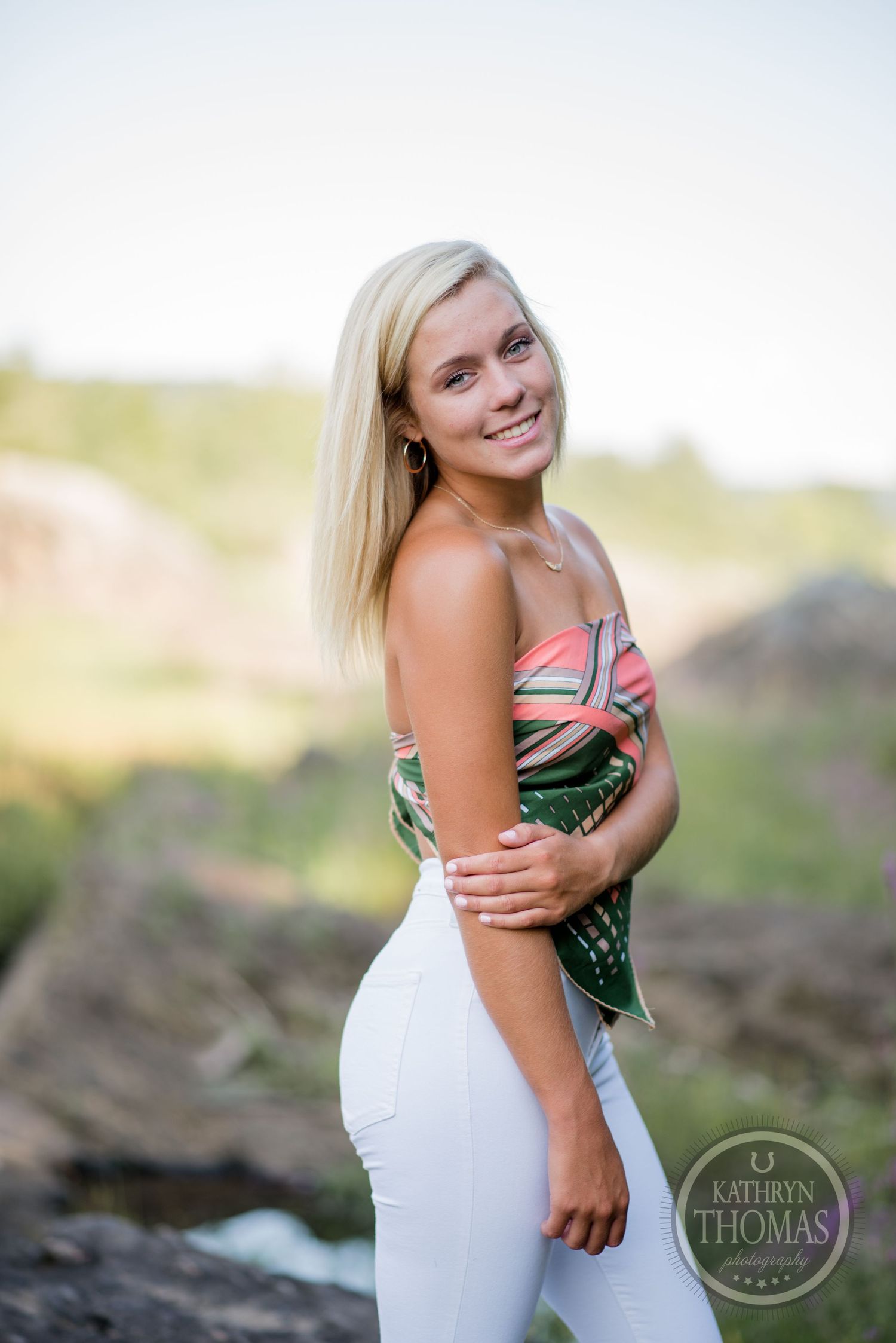 Summer portrait showing someone in patterned top and white pants against natural background.