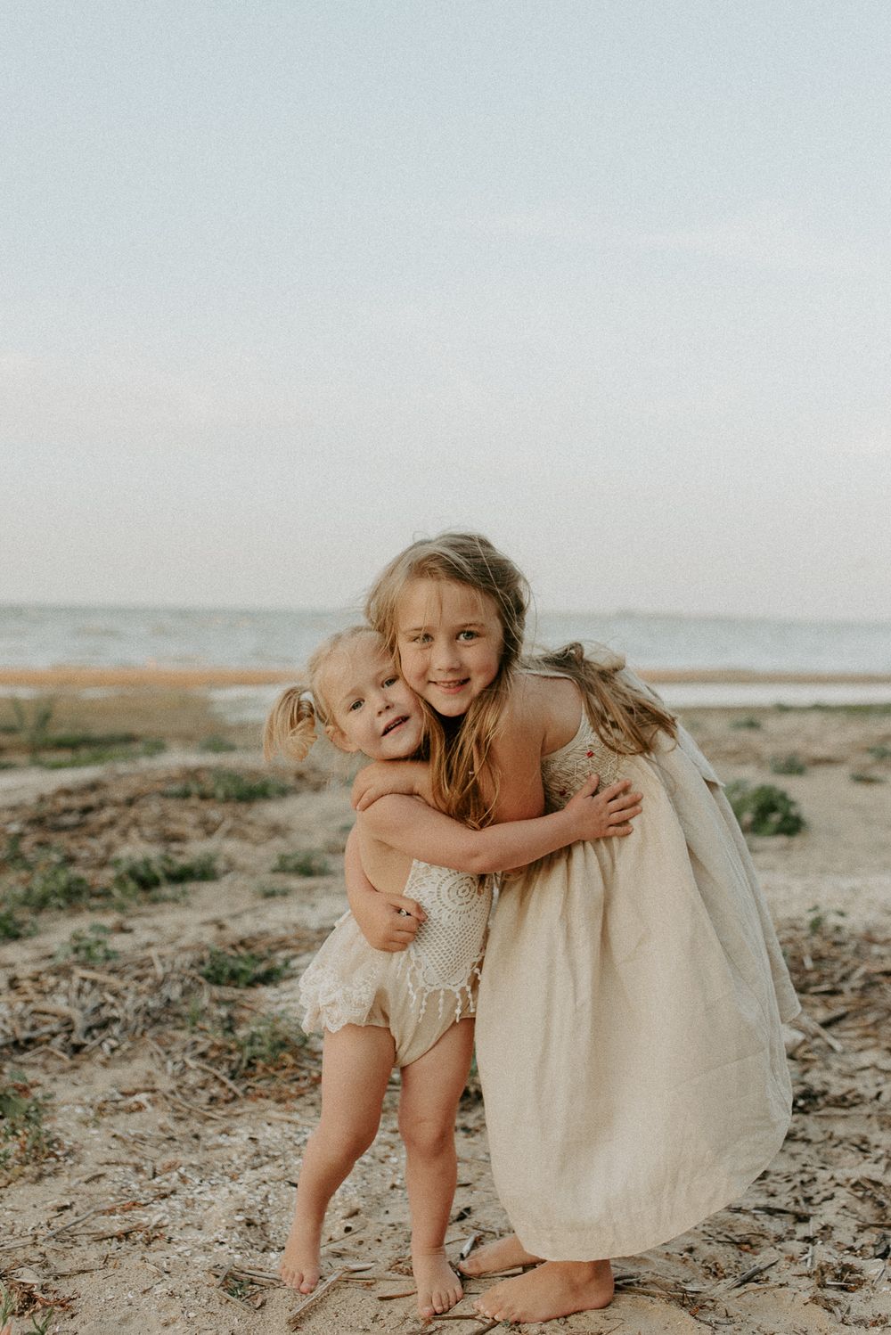 Joyful embrace shared on a sandy beach at sunset with light cream colored dress.