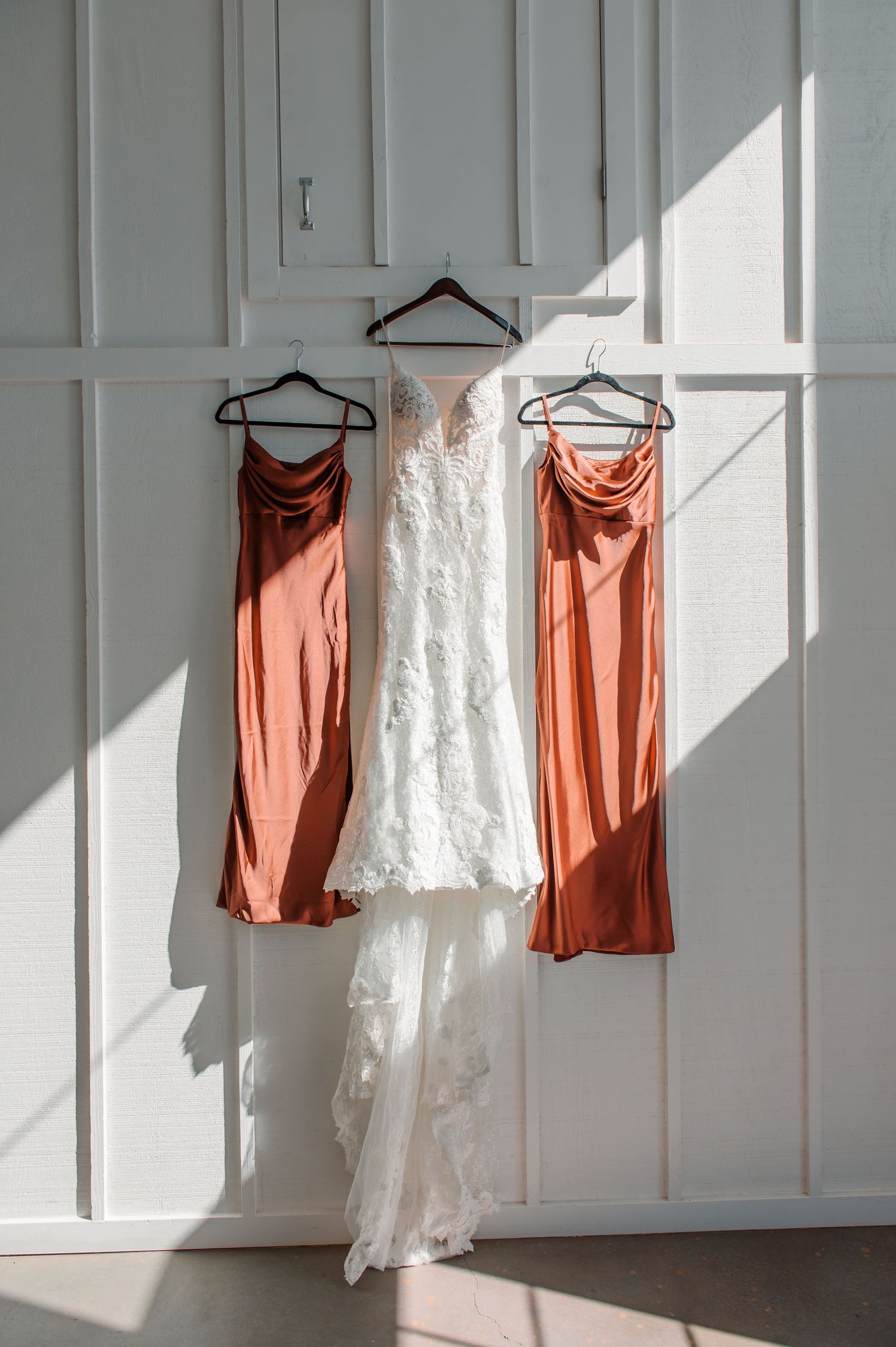White and coral colored clothing hanging on white paneled walls in natural light.