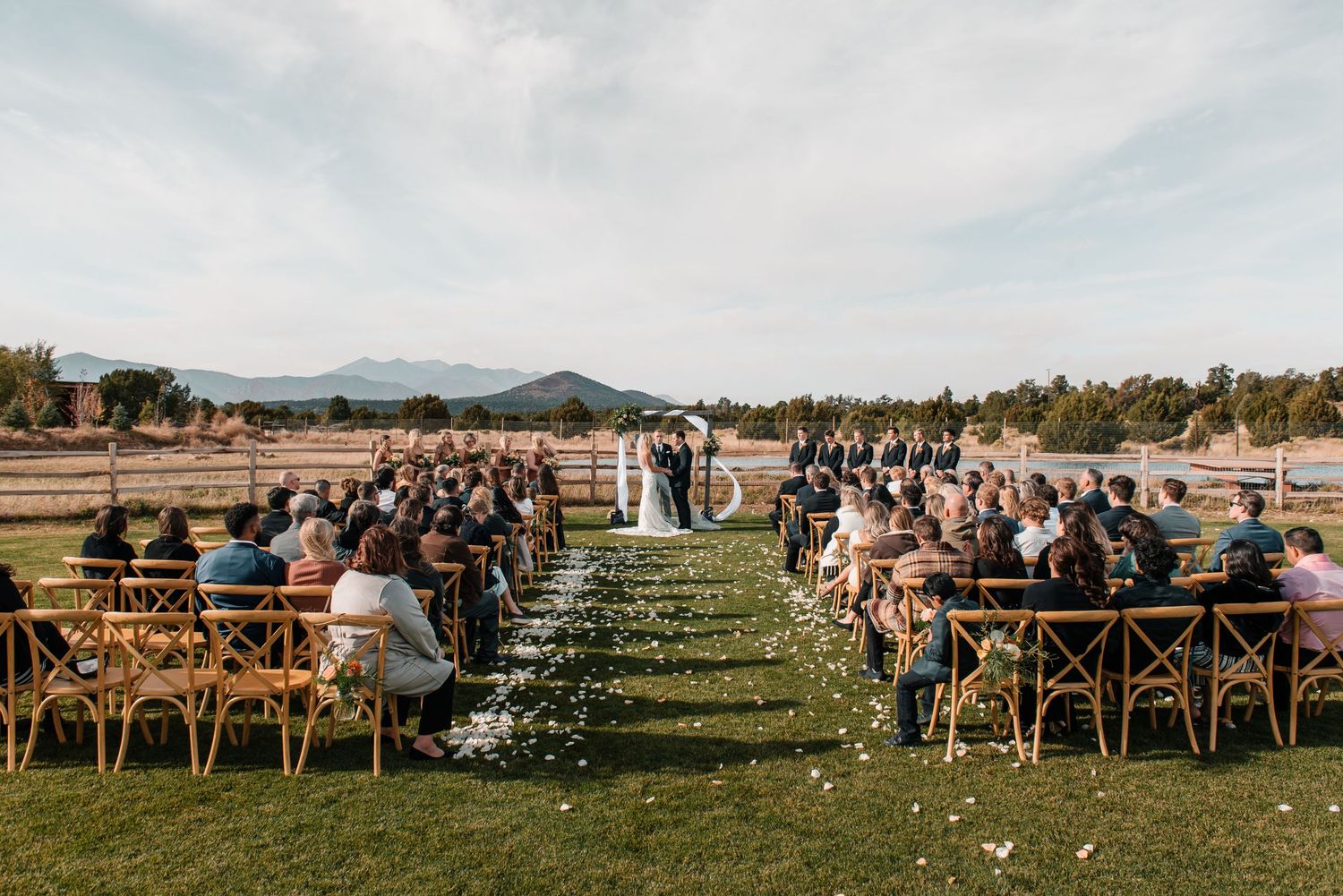 Wide angle shot of wedding guests seated in rows during an outdoor ceremony with mountain backdrop.
