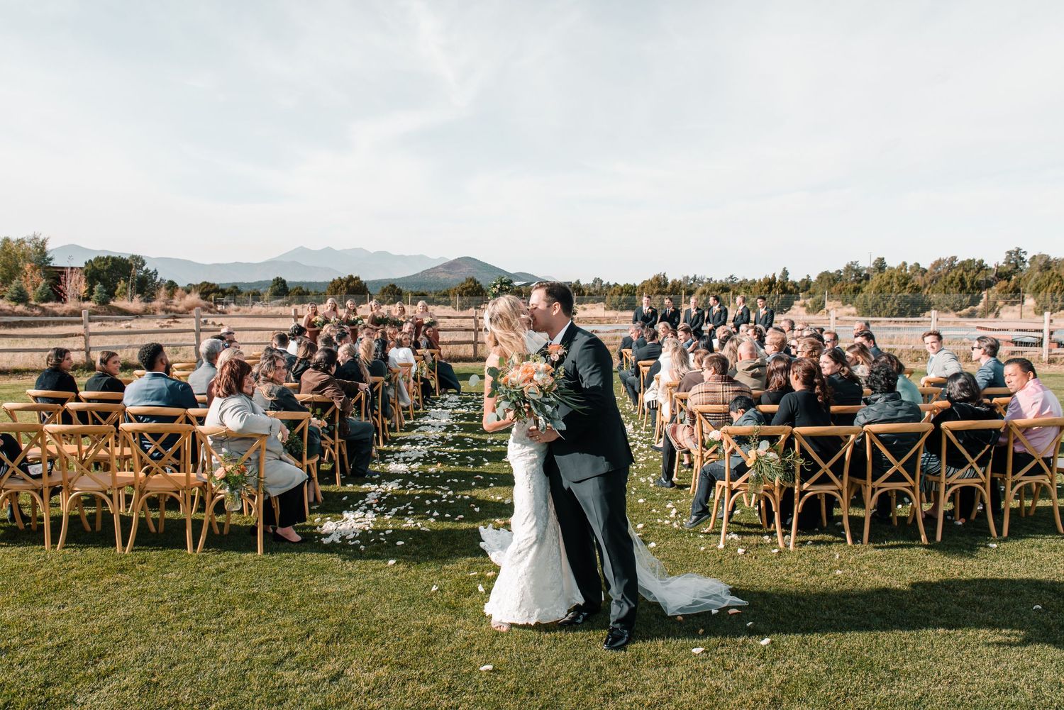 Scenic outdoor wedding ceremony with wooden cross-back chairs and mountain landscape.