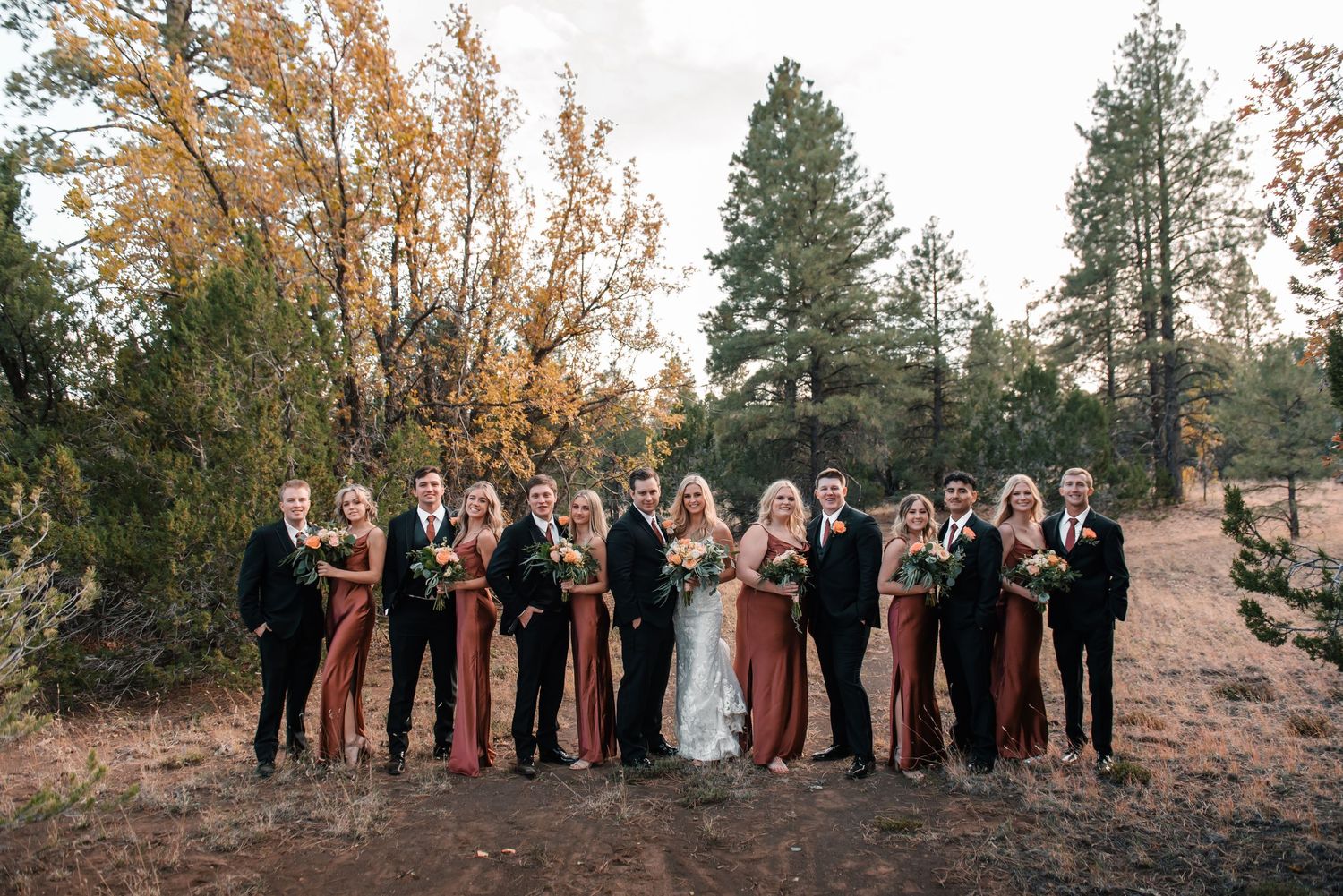 Wedding party posing together against autumn trees and mountain landscape.