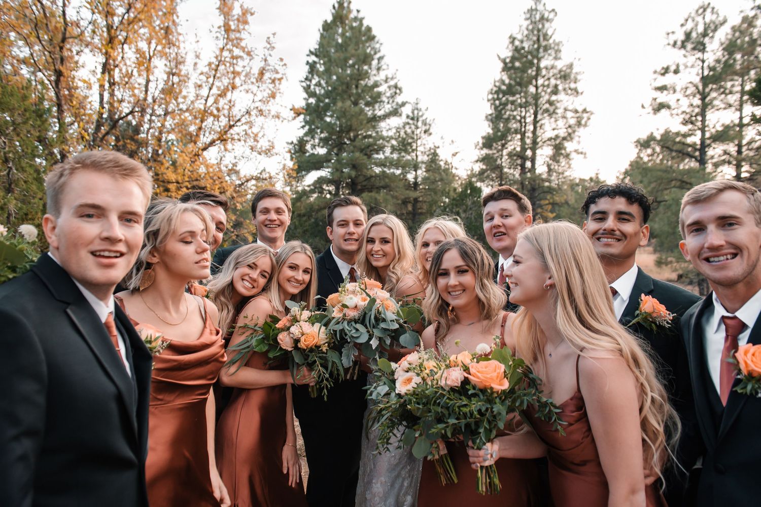 Wedding party laughs together outdoors with bridesmaids in burgundy dresses.