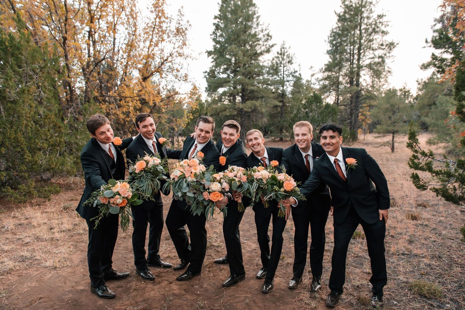 Wedding party members line up on natural terrain with evergreen trees behind them.