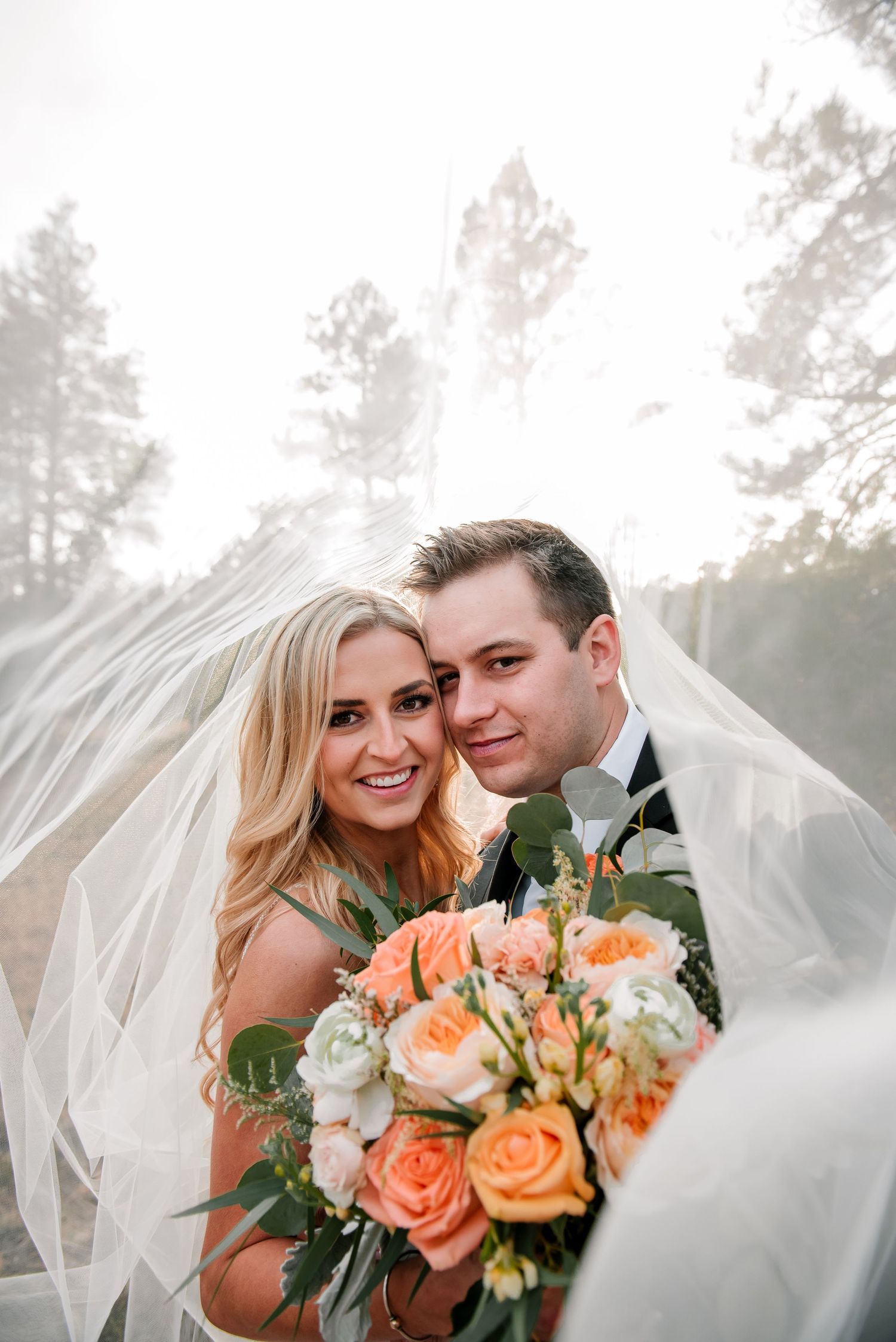 Romantic wedding portrait with peach roses and flowing veil in natural light.