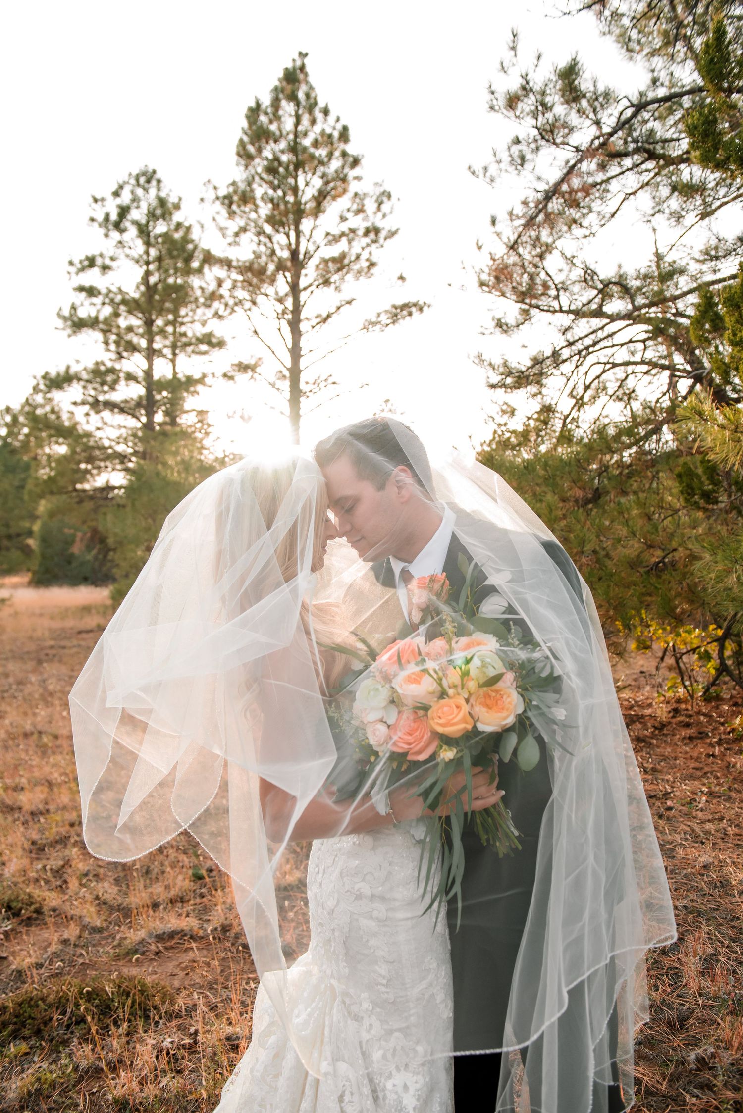 Ethereal bridal portrait with flowing veil and peach rose bouquet at sunset.