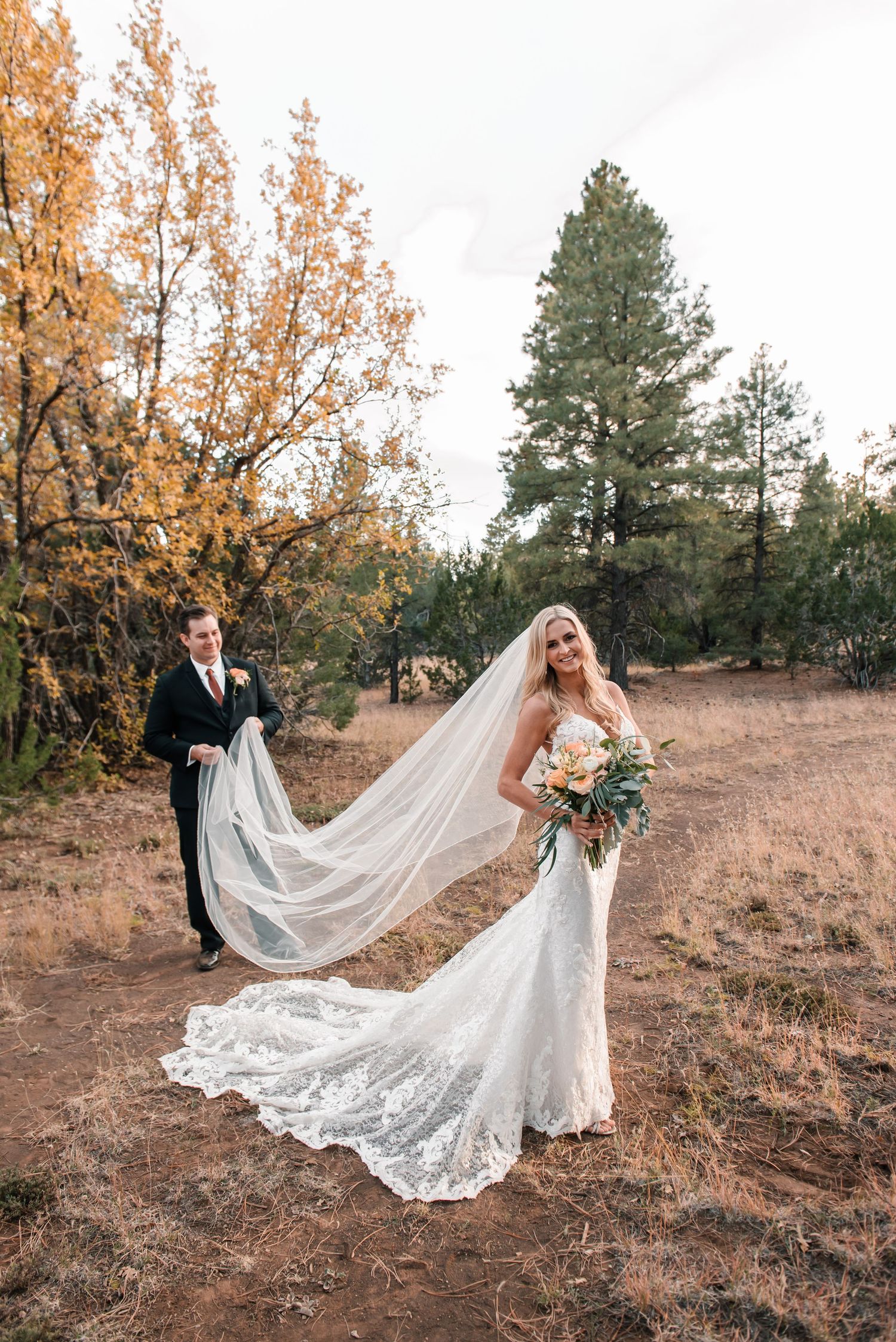 A flowing lace wedding dress with dramatic veil captured in a fall outdoor setting.