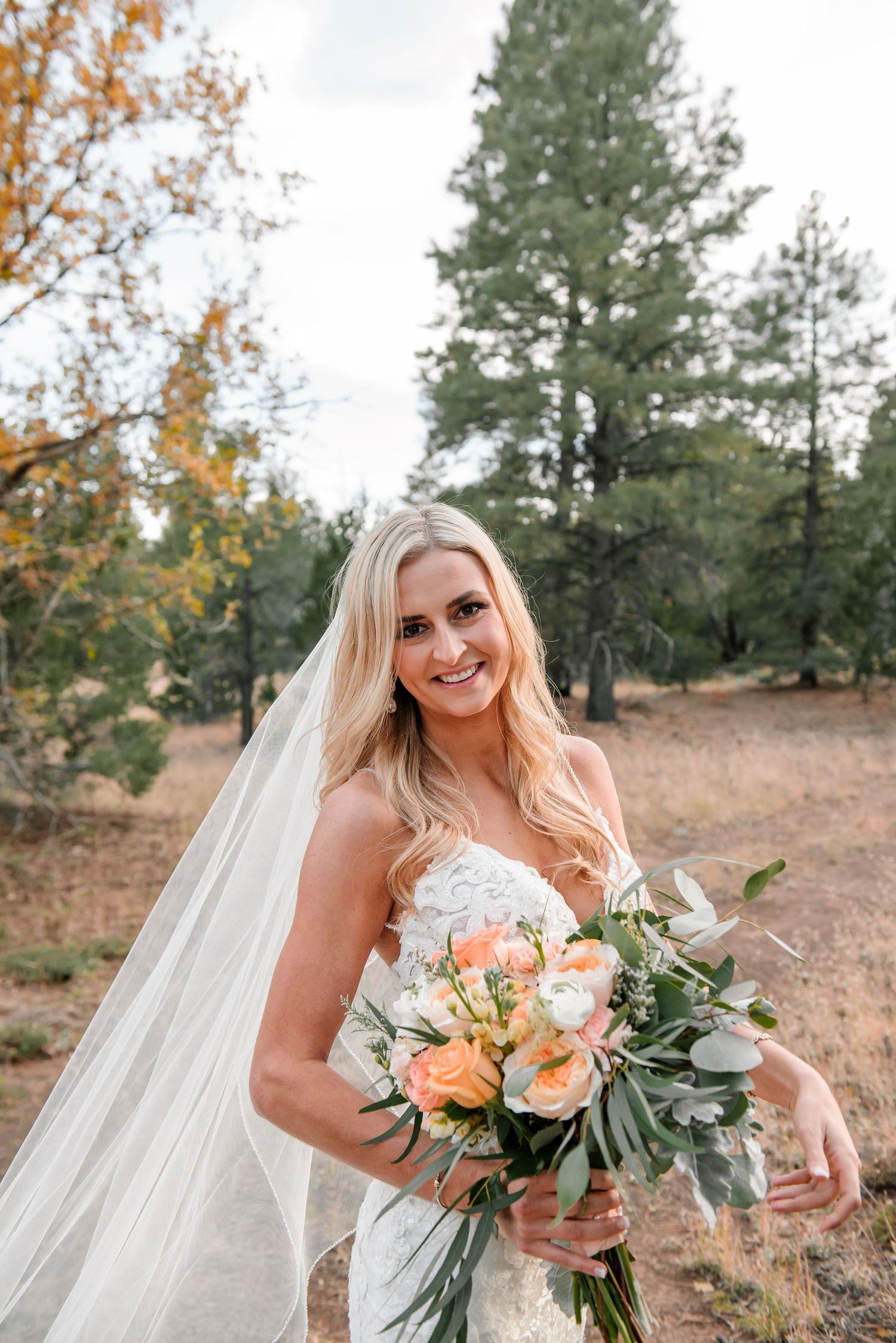 A stunning bridal bouquet featuring peach roses and eucalyptus leaves against an autumn backdrop.
