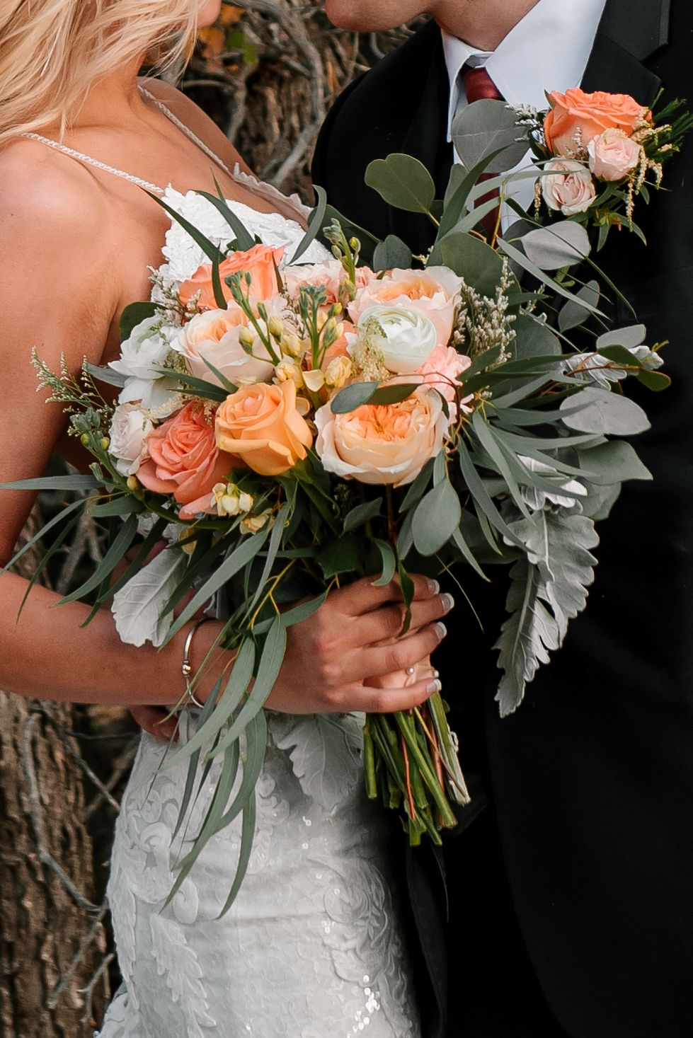 Wedding bouquet featuring peach roses and eucalyptus leaves against formal attire.