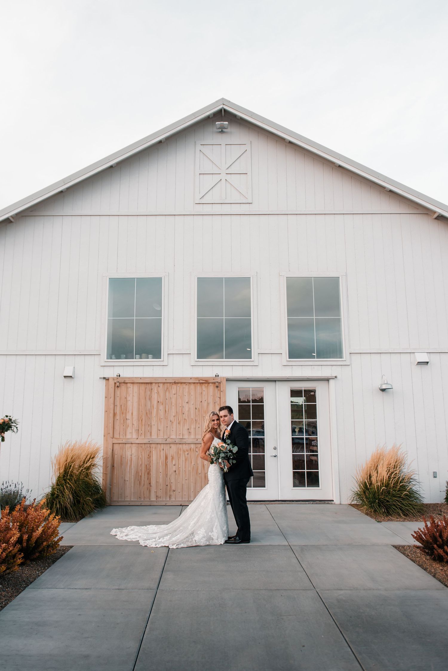 Modern white barn wedding venue with glass doors and ornamental grasses.