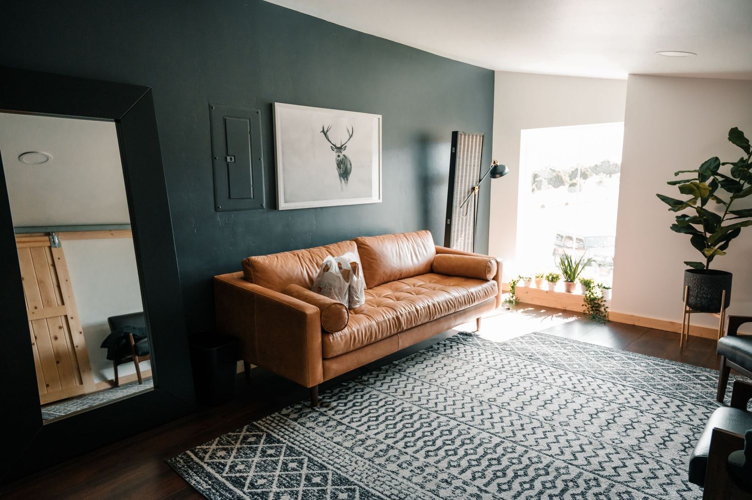 Modern living room with teal wall, tan leather couch, and geometric rug.